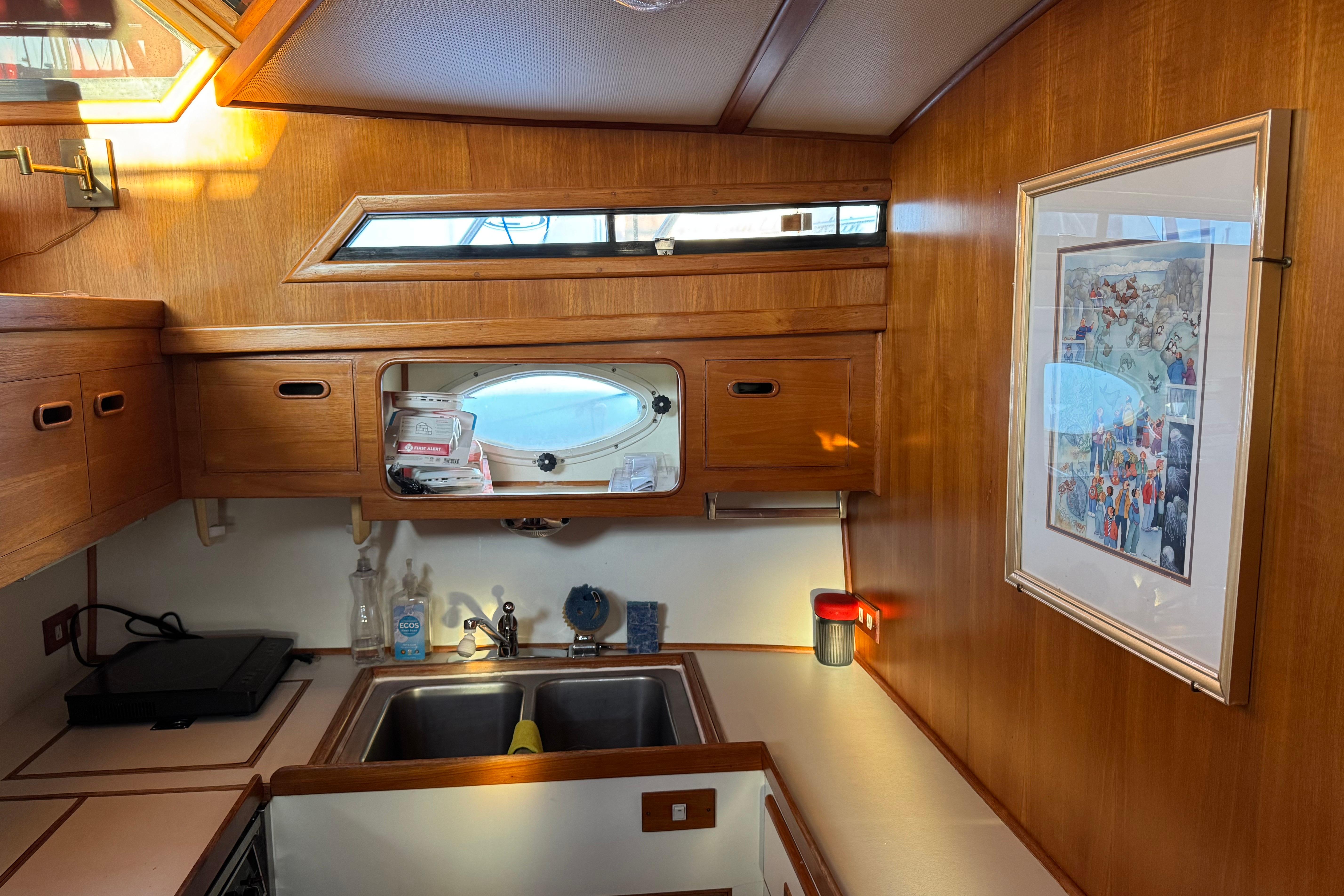 Wood-paneled kitchen interior of 1987 President 37 yacht with framed artwork and porthole window.