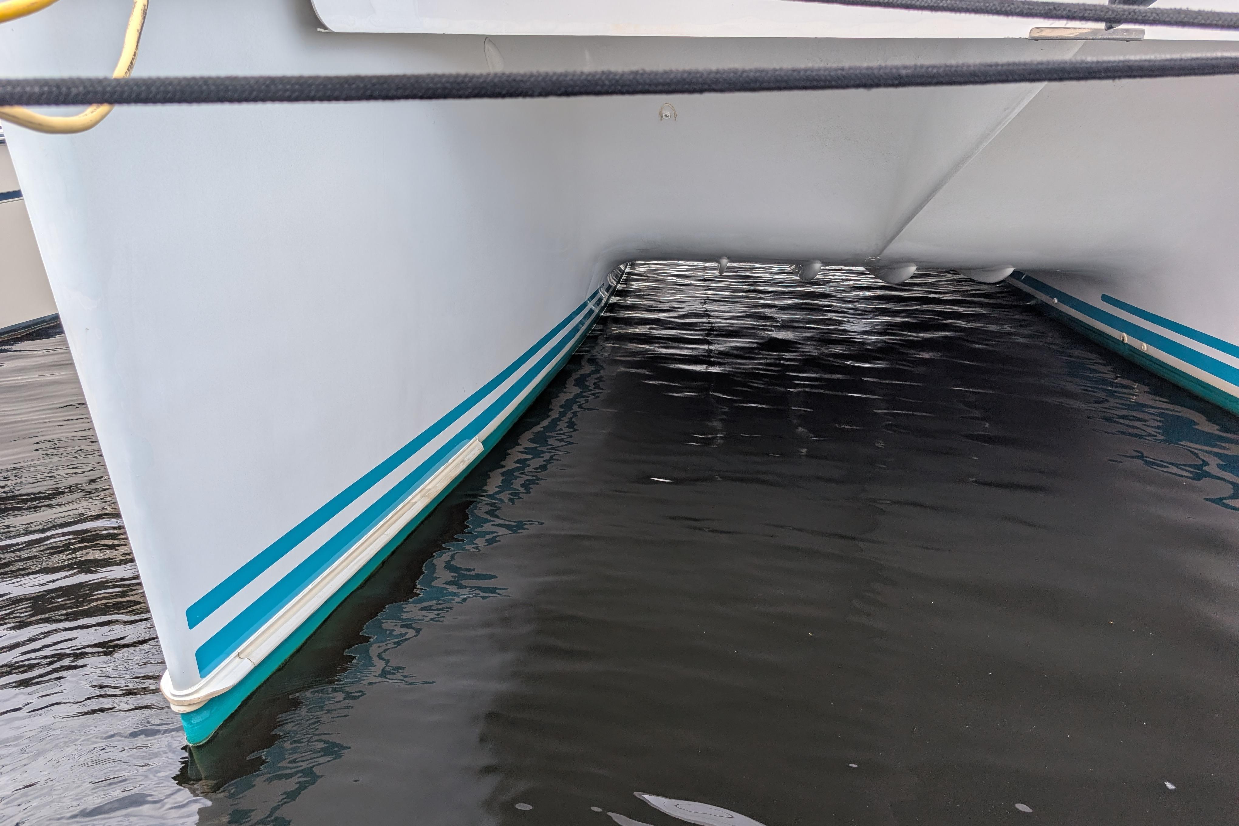 2004 PDQ 34 Powercat catamaran hull with blue stripes on calm water.