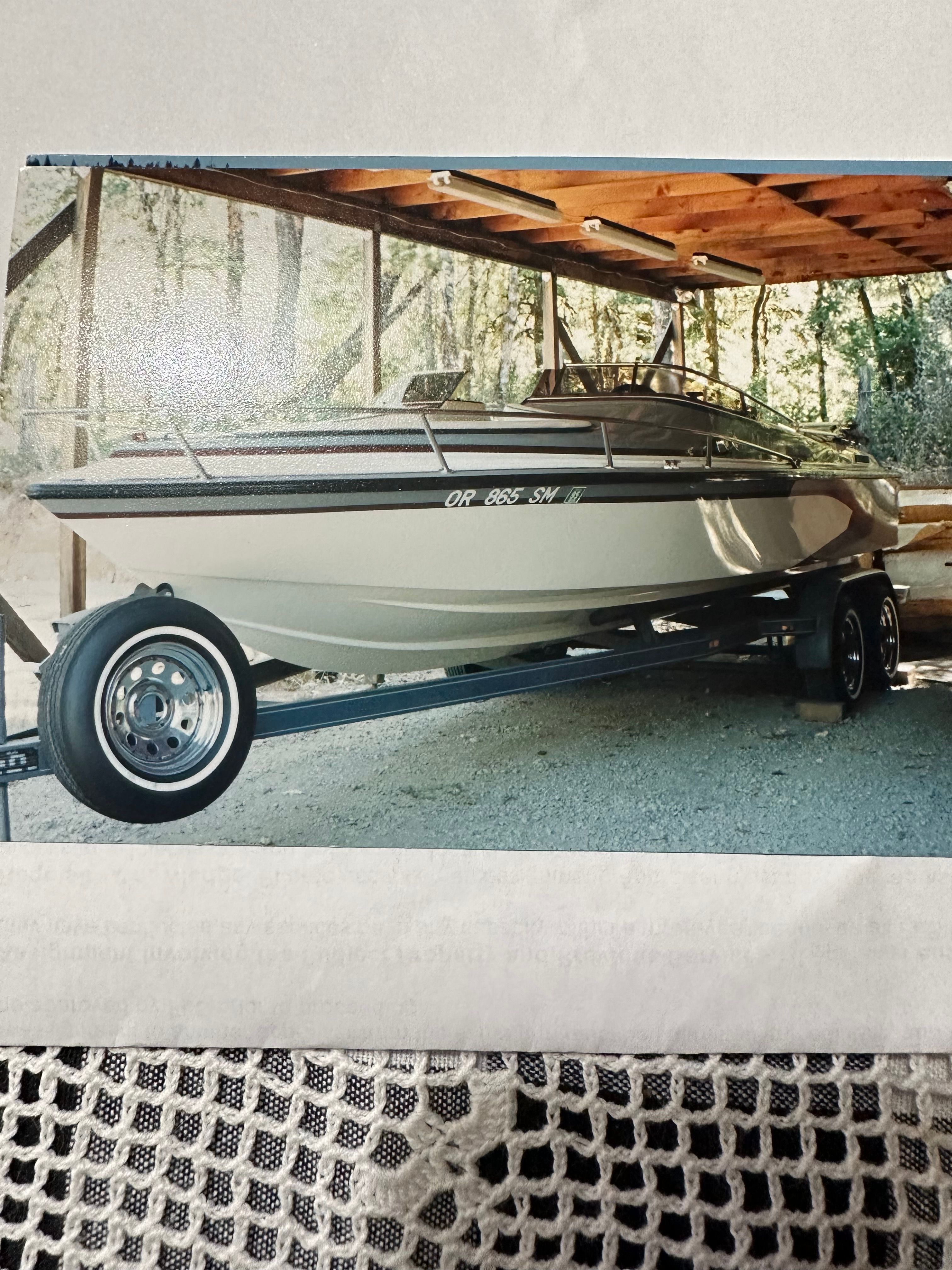 A 1990 Marlin Open Bow boat on a trailer under a wooden shelter.