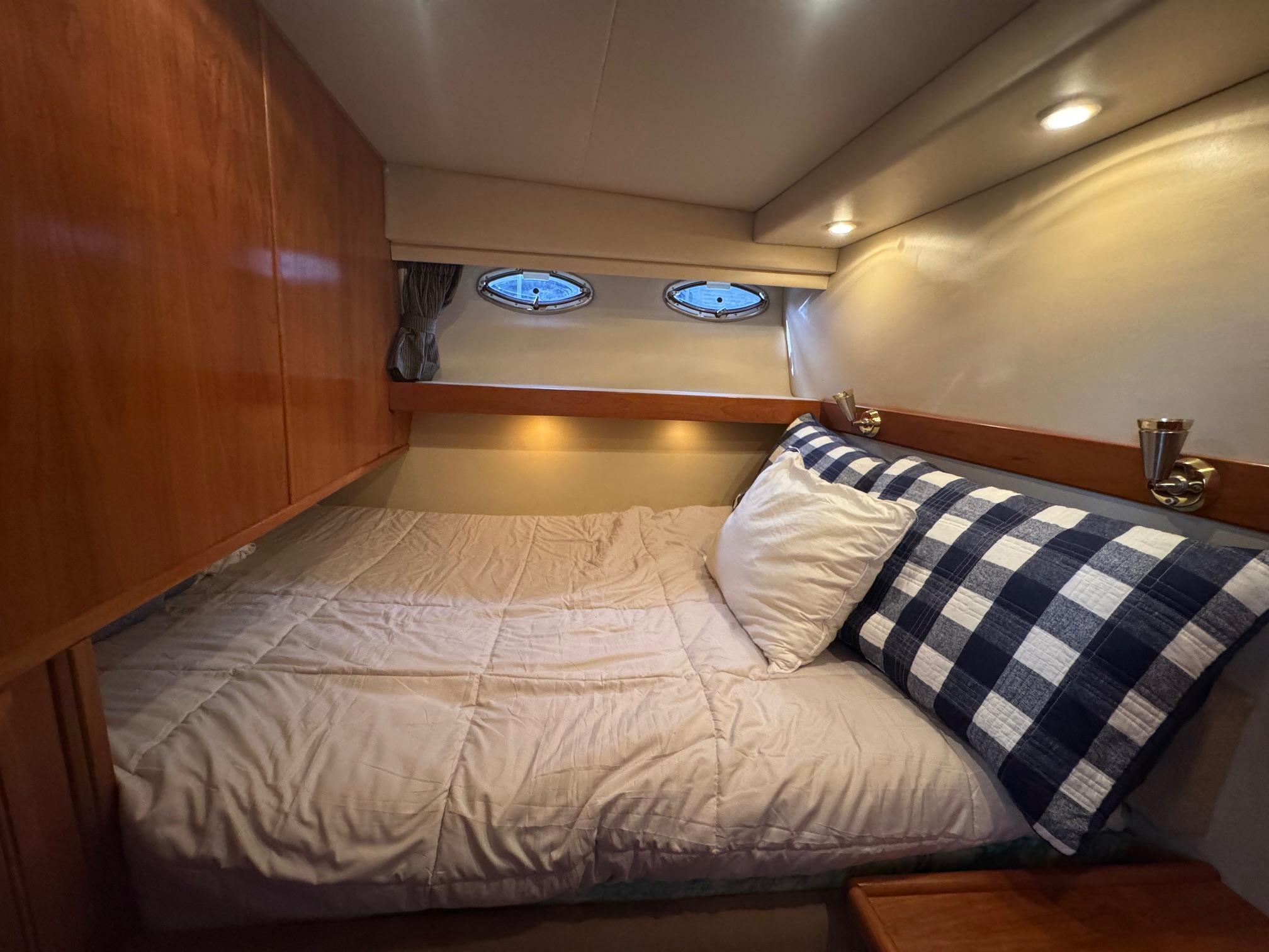 Cozy bedroom in 2004 Meridian 490 Pilothouse yacht with wood cabinets and porthole windows.
