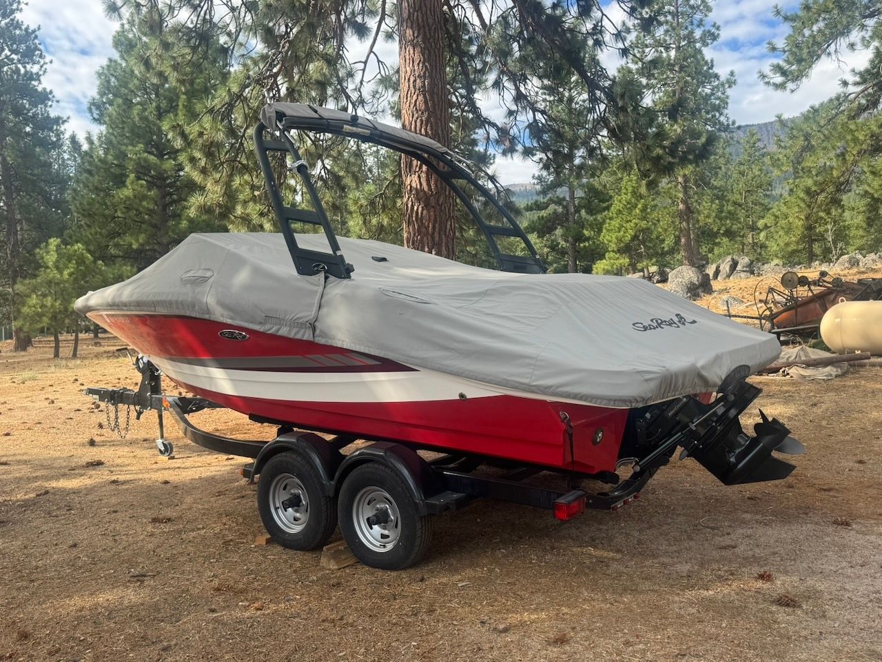 A red 2016 Sea Ray SPX 190 Outboard boat on a trailer in a wooded area.
