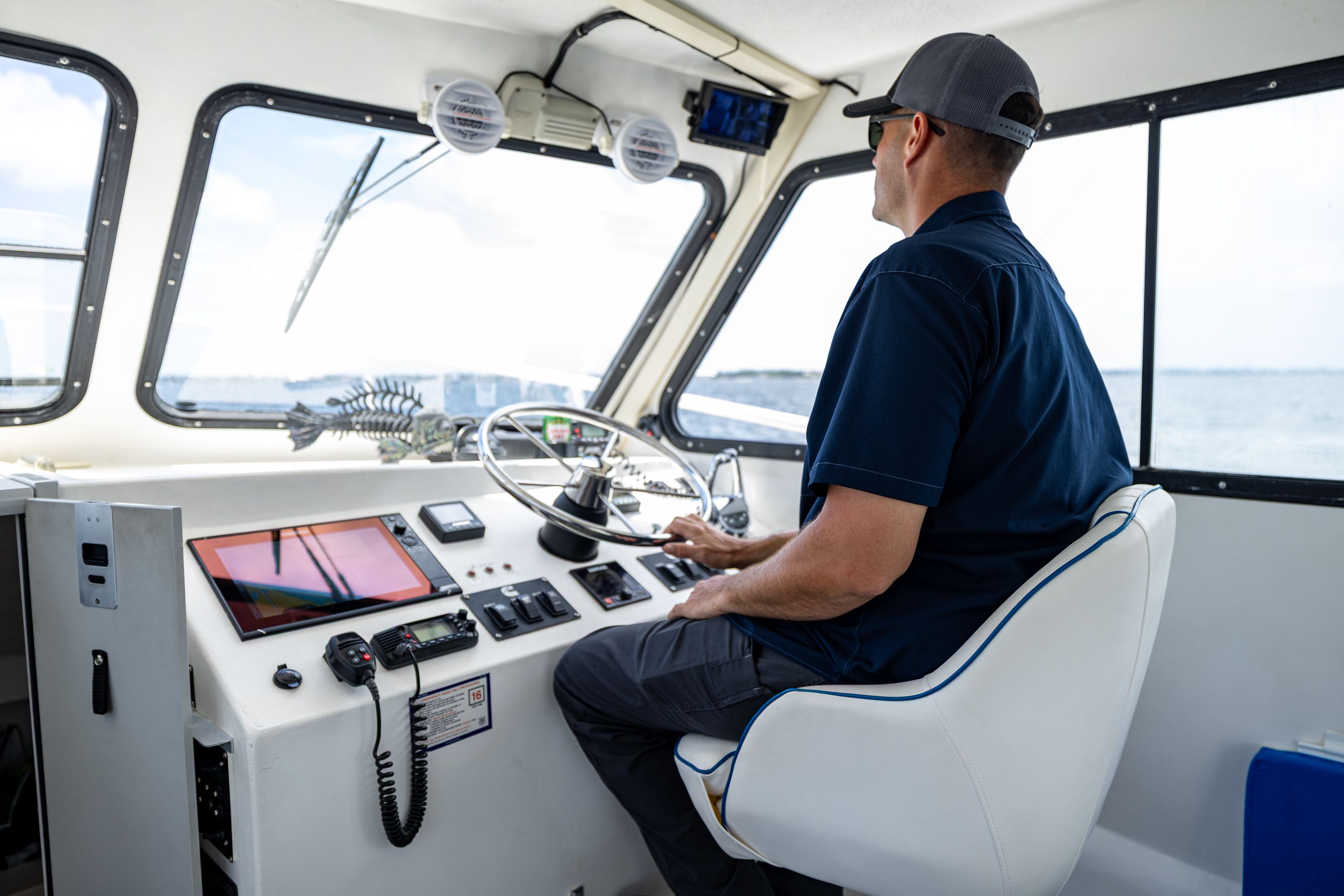 A man navigates a boat from the cabin, overlooking the sea.