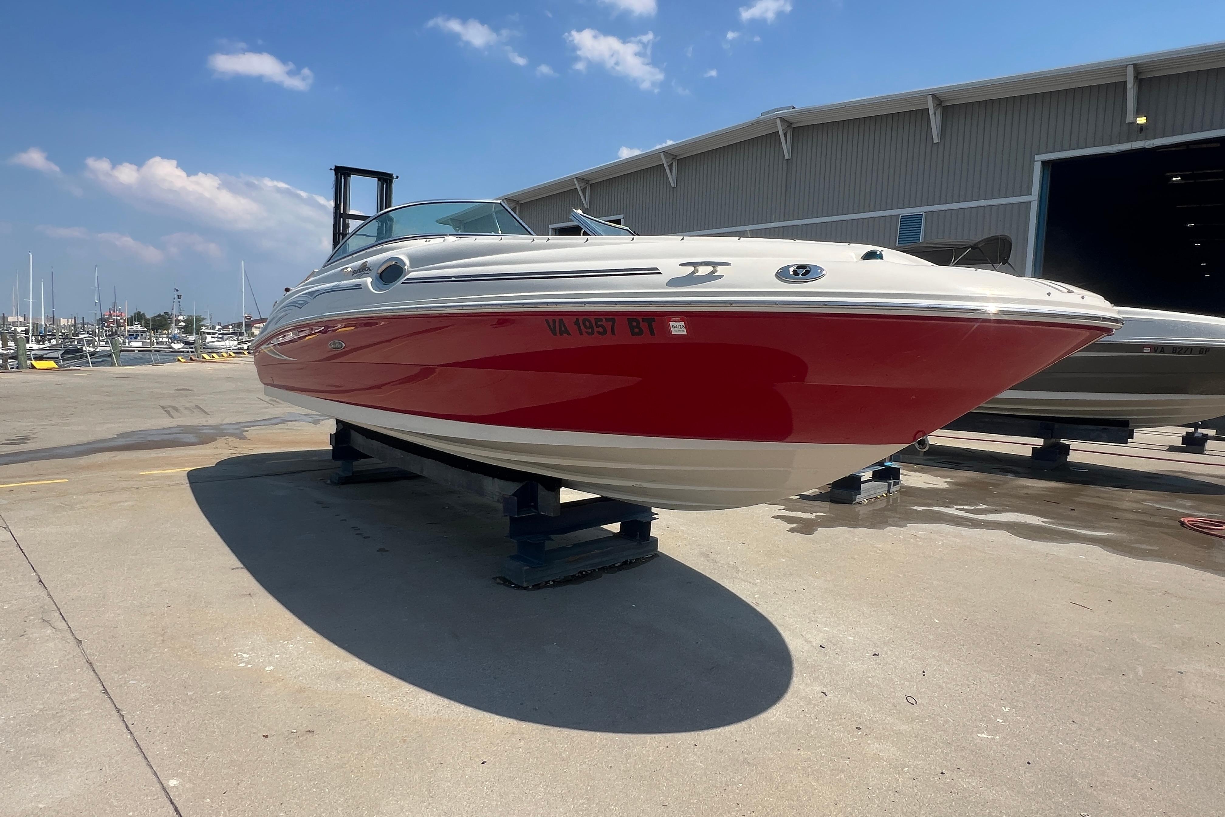 2005 Sea Ray 240 Sundeck boat with red hull, docked at marina under blue sky.