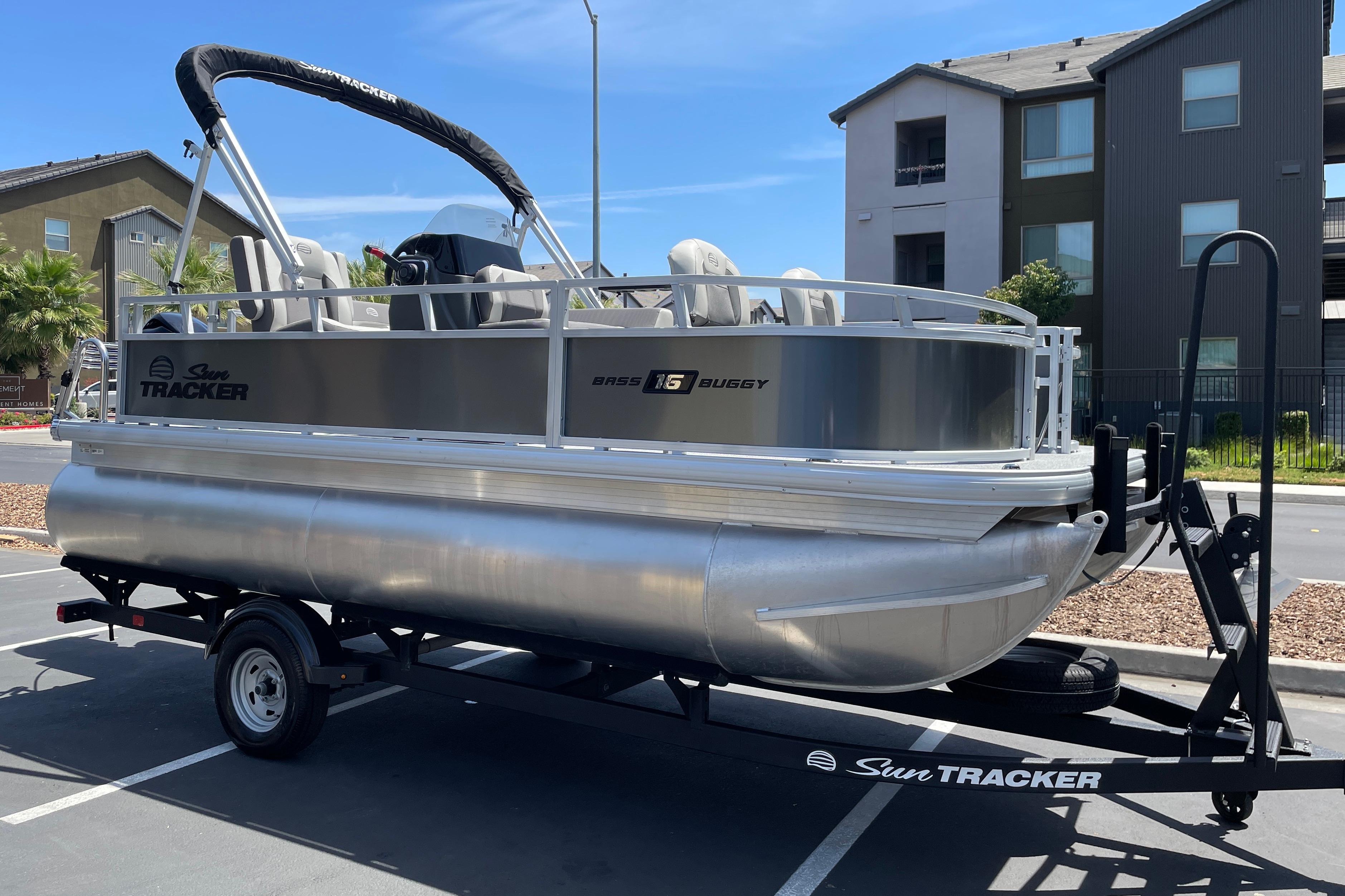 2026 Sun Tracker Bass Buggy 16 XL Select pontoon boat on trailer in parking lot.