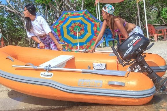 Two people with an orange Caribe L-9 inflatable boat, 2025 model, on a sunny beach.