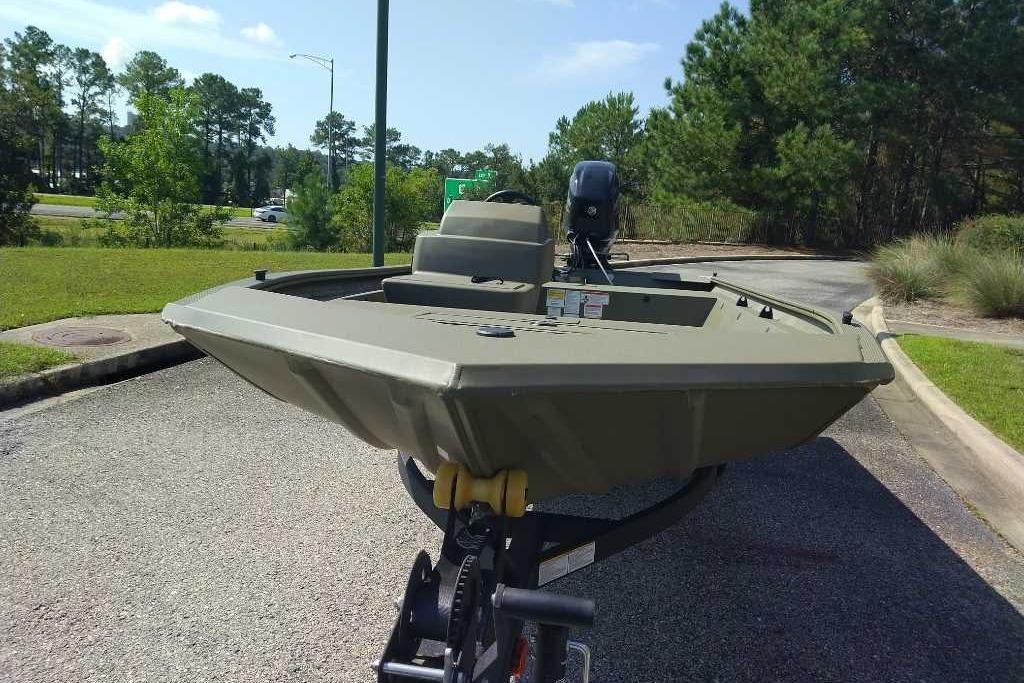2026 Tracker Grizzly 1648 SC boat on trailer, parked outdoors, surrounded by trees.