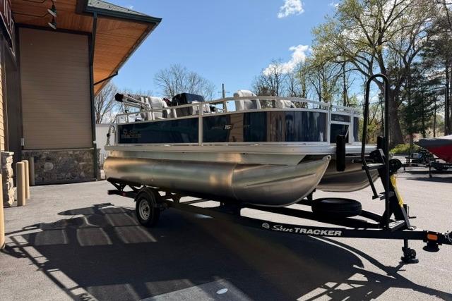 2026 Sun Tracker Bass Buggy 16 XL Select pontoon boat on trailer, parked outdoors.