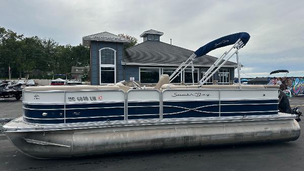 A 2018 South Bay S224CR pontoon boat is parked on a lot in front of a building.