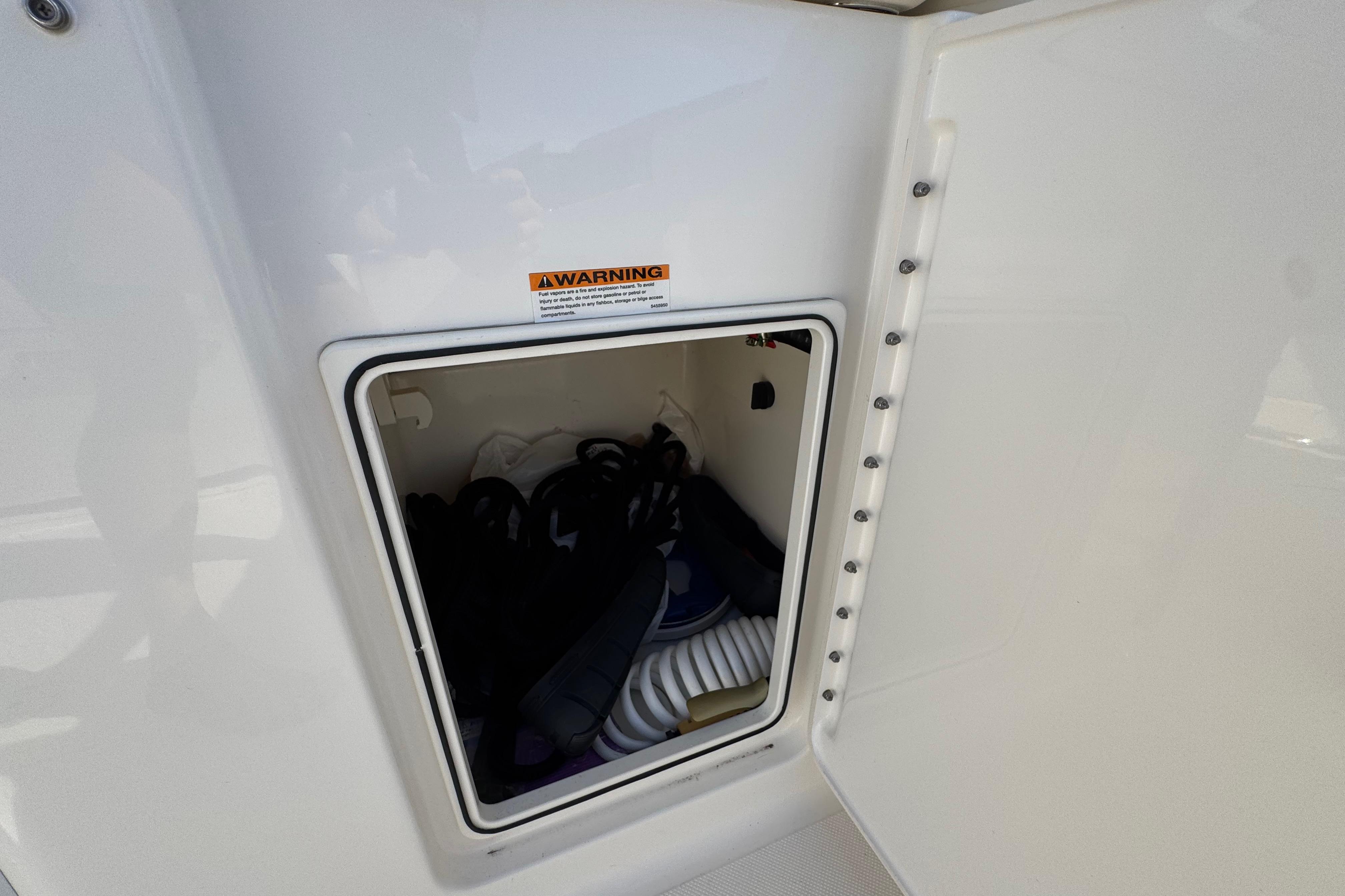Storage compartment on 2022 Pursuit DC 266 Dual Console boat, containing coiled hose and gear.