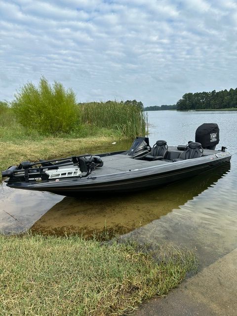 A 2023 Skeeter FXR21 Apex boat is docked by the shore of a calm lake.
