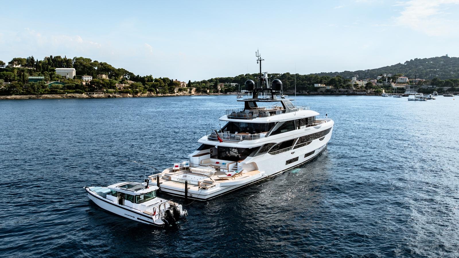 2024 Axopar 37 XC Cross Cabin boat cruising near a luxury yacht on a scenic coastline.