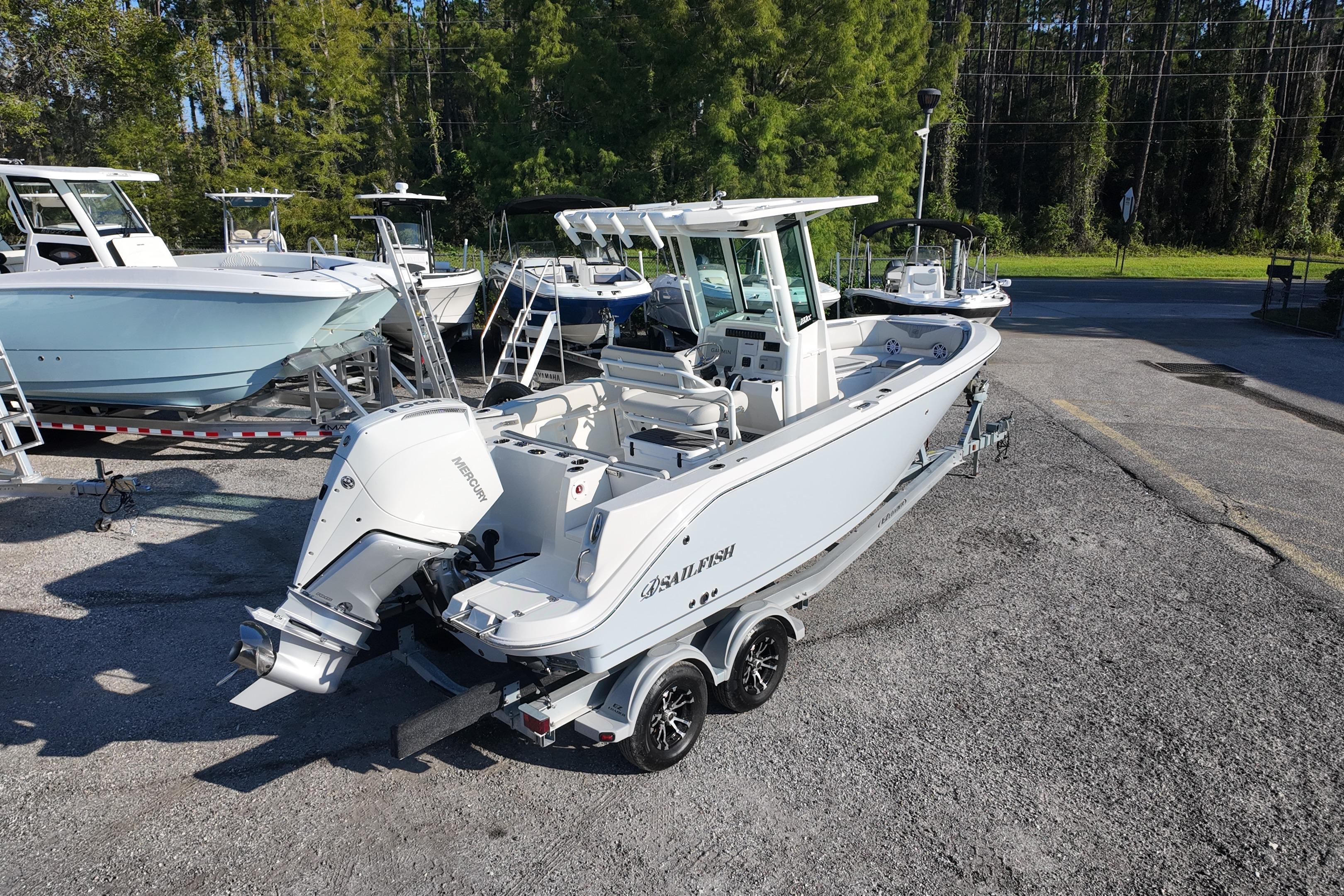 2026 Sailfish 232 CC boat on trailer, parked outdoors, surrounded by trees and other boats.