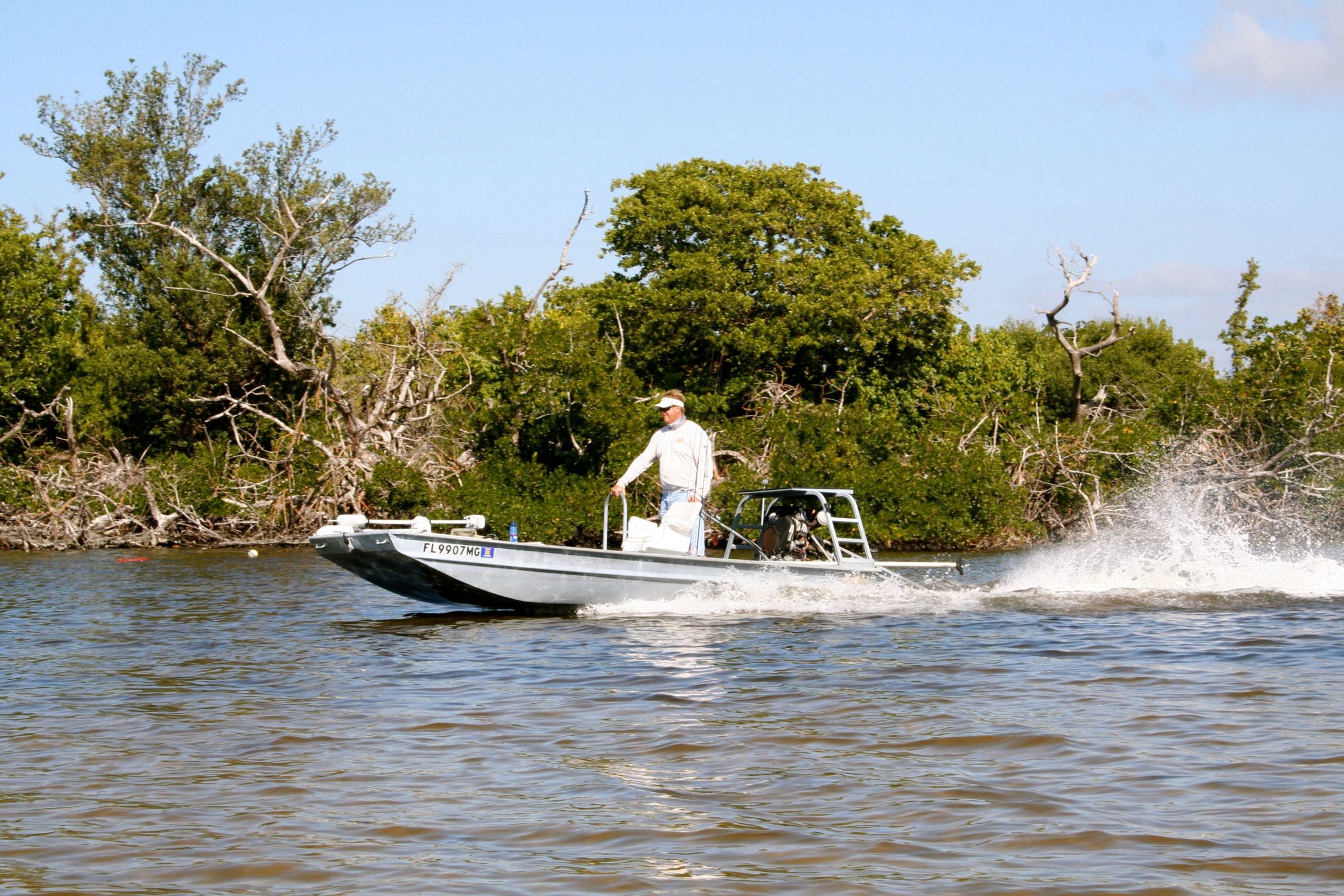 An angler navigates a Go-Devil 16x56 boat on a river, surrounded by trees.