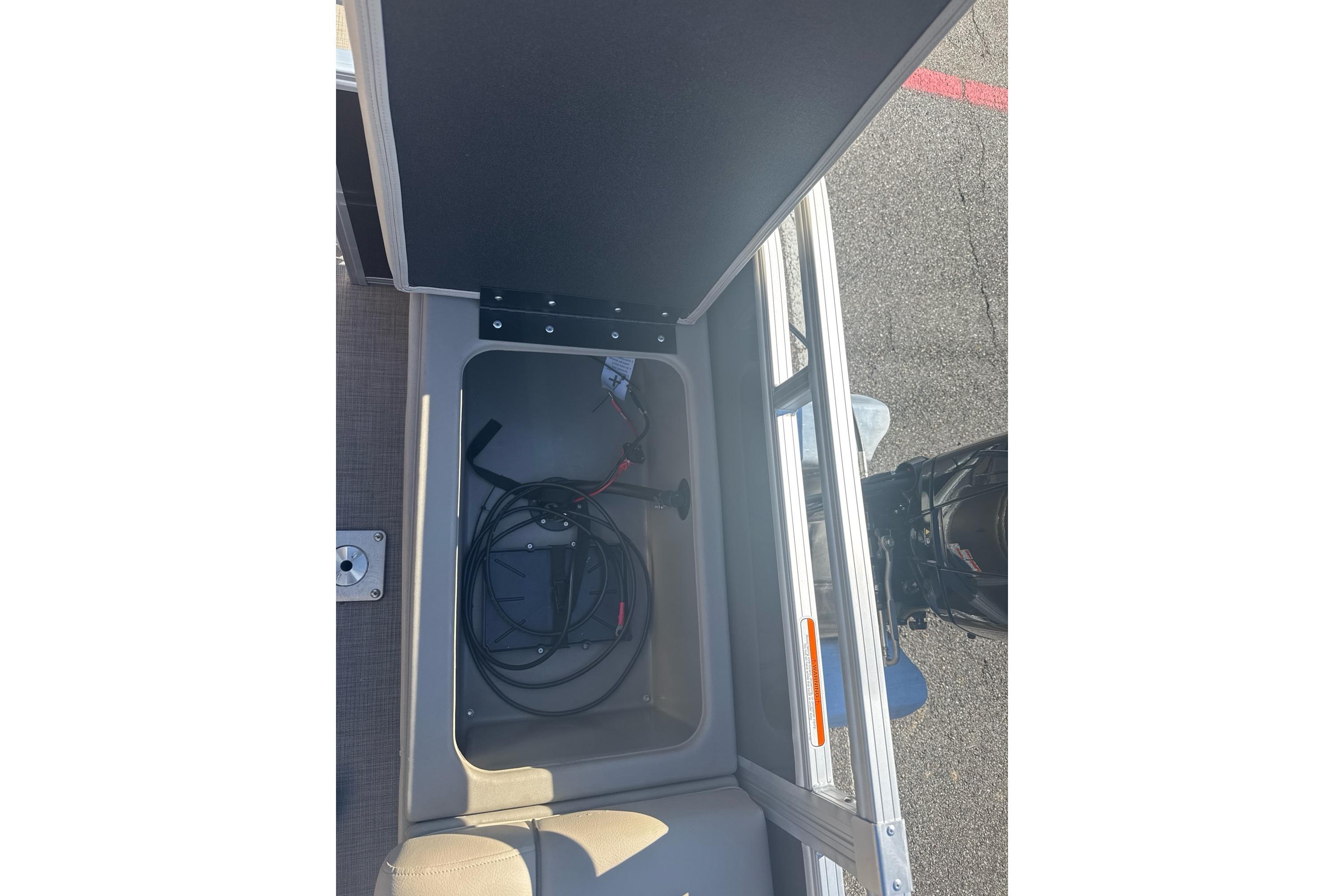 Open storage compartment on 2025 Sun Tracker SportFish 22 DLX boat with cables inside.