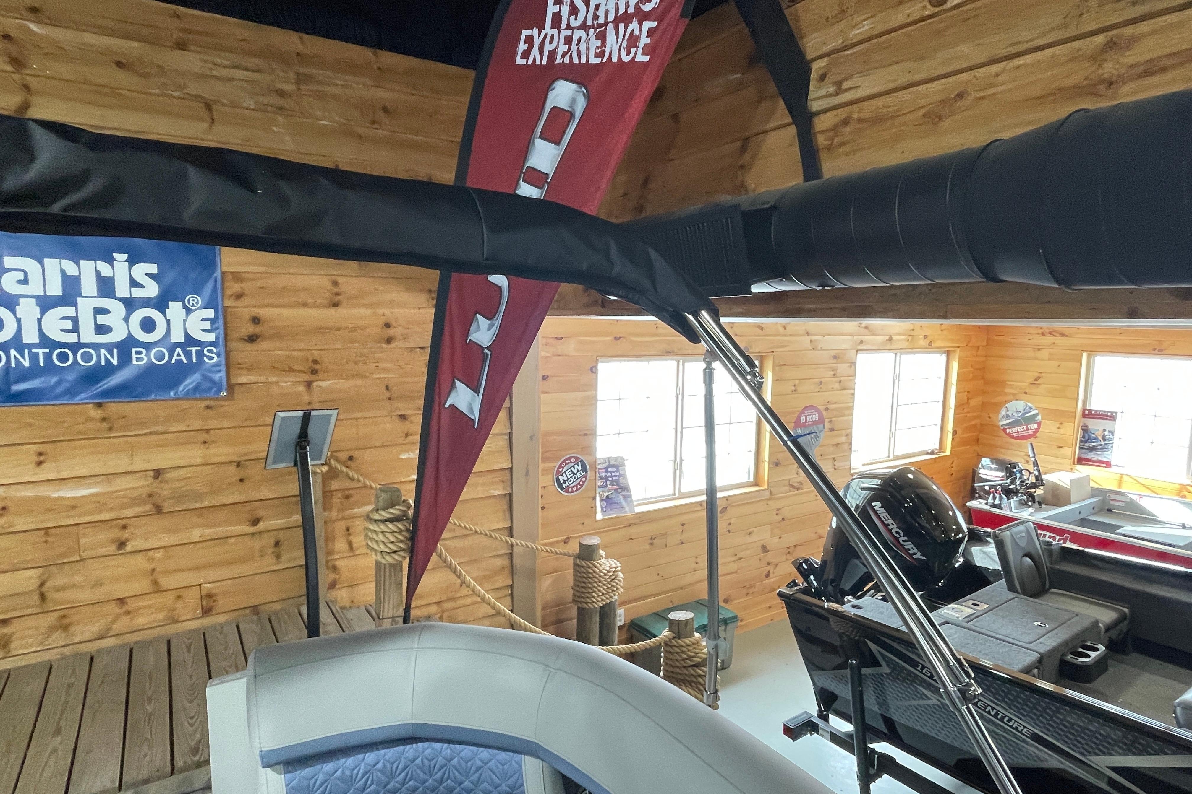 2026 Harris Grand Mariner SLEC 250 pontoon boat in wooden showroom with promotional banners.