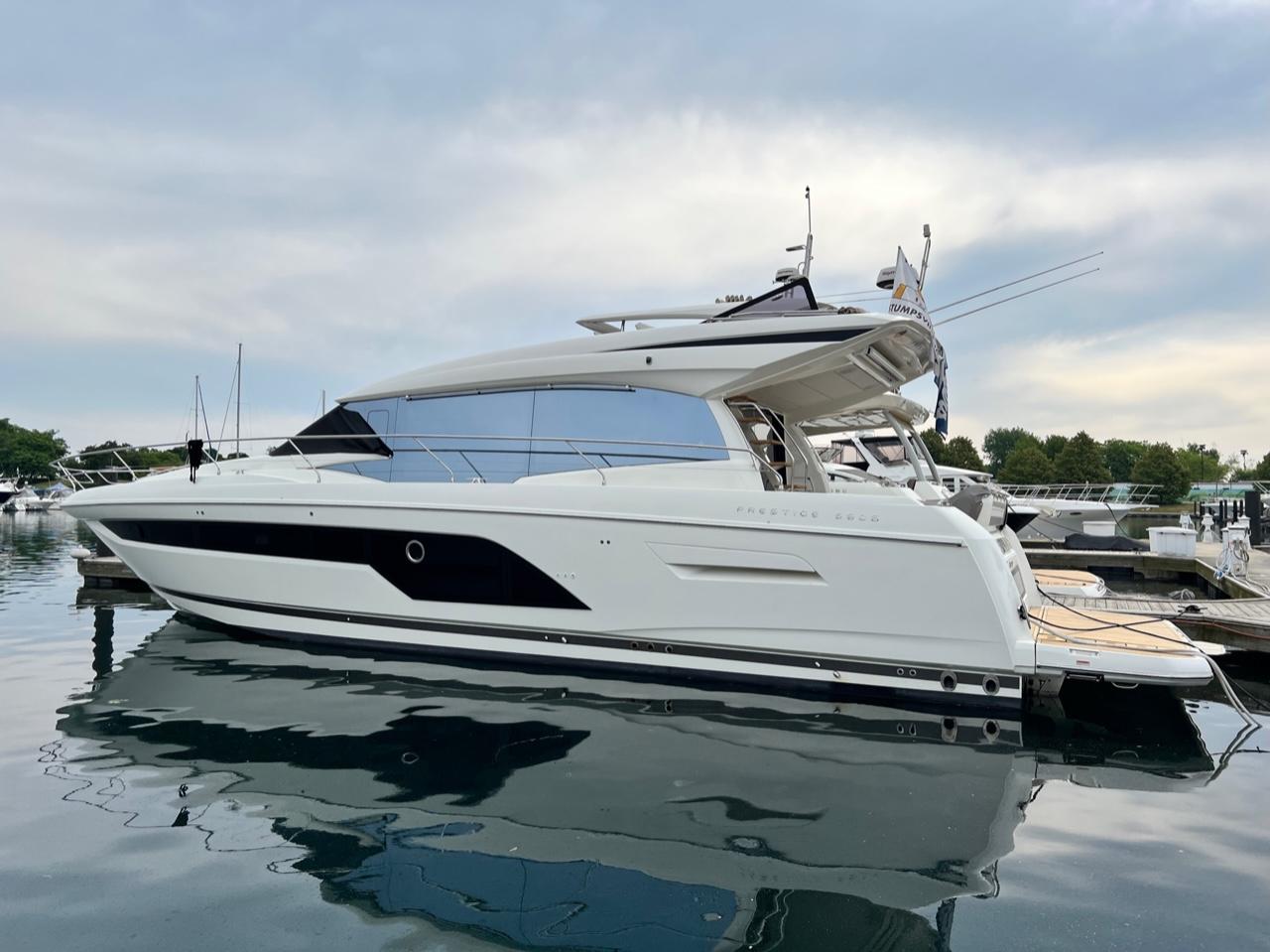 2021 Prestige 590 Sport Fly yacht docked in a marina, reflecting on calm water.
