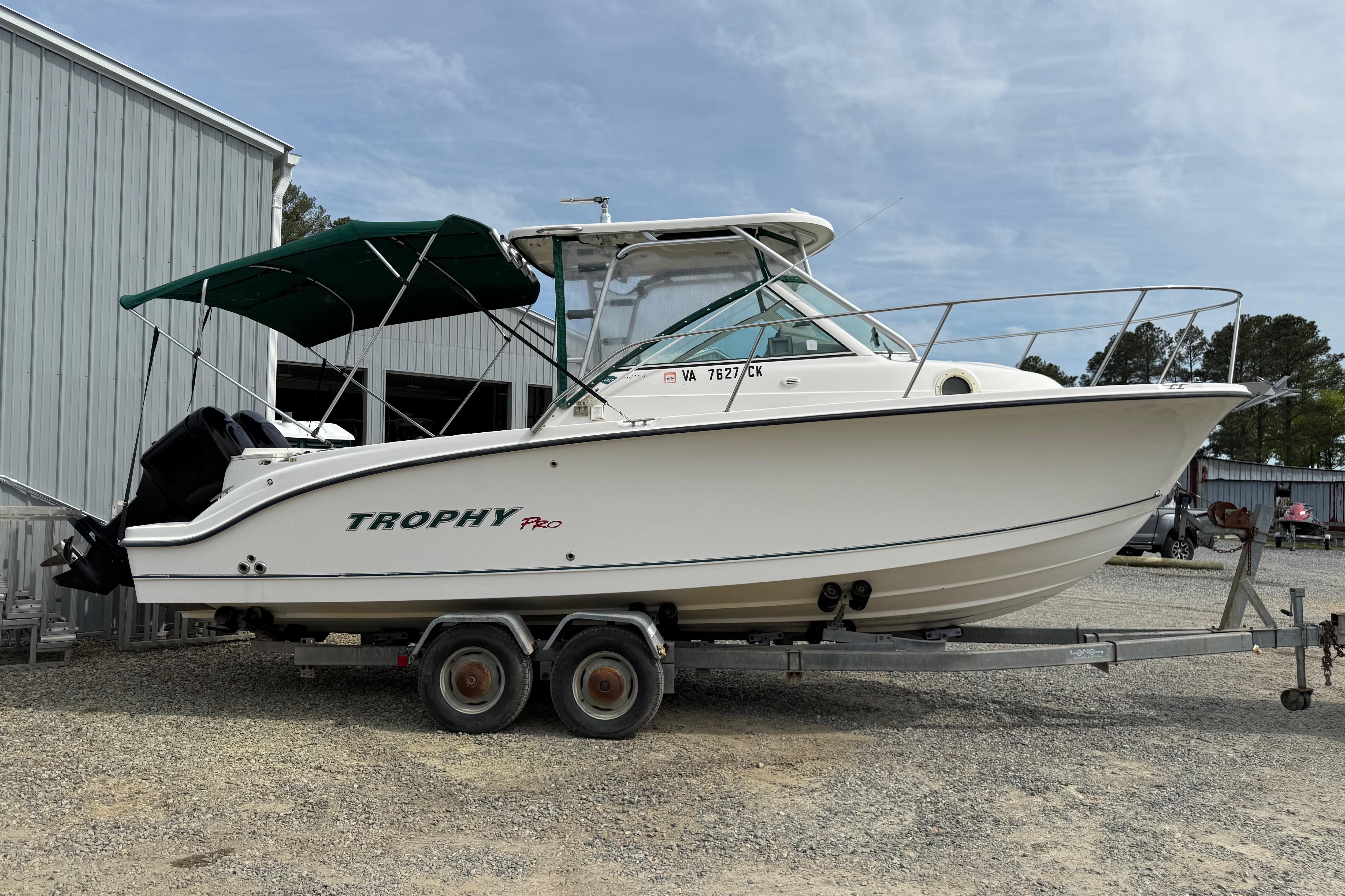 2006 Trophy 2502 Walkaround boat on trailer, parked near a metal building.