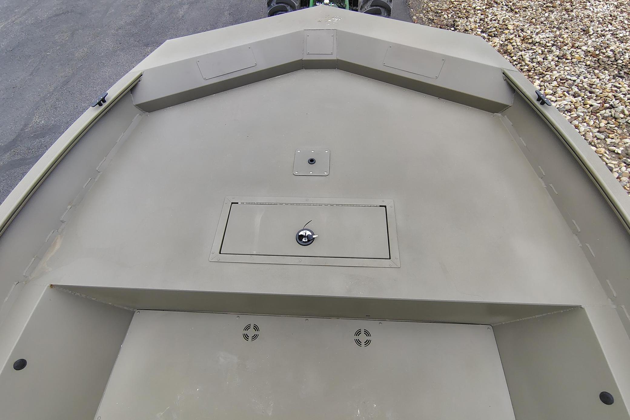 2026 Tracker Grizzly 2072 Utility boat deck with storage compartment, shown on a gravel surface.