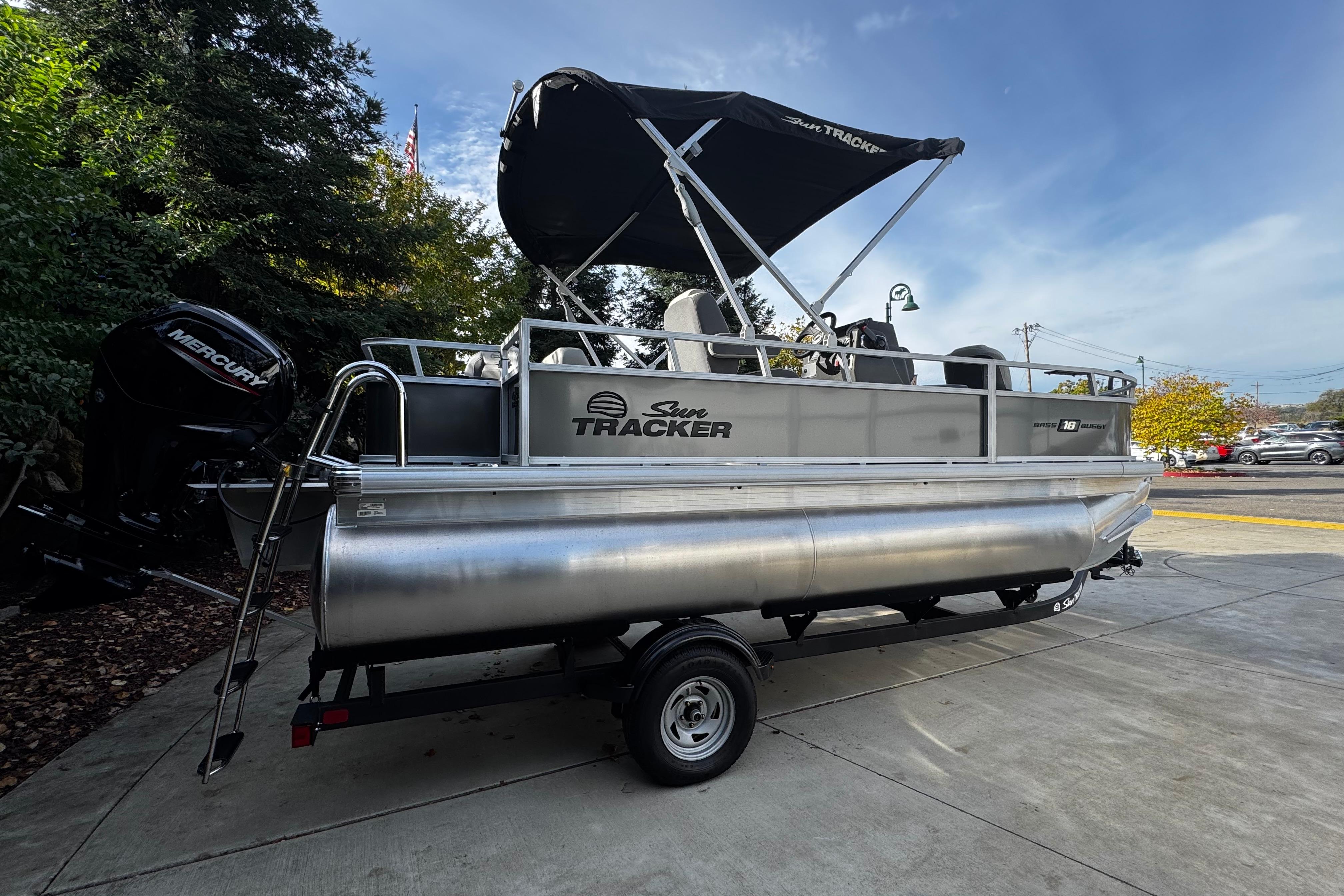 2026 Sun Tracker Bass Buggy 18 DLX pontoon boat on trailer, parked outdoors.