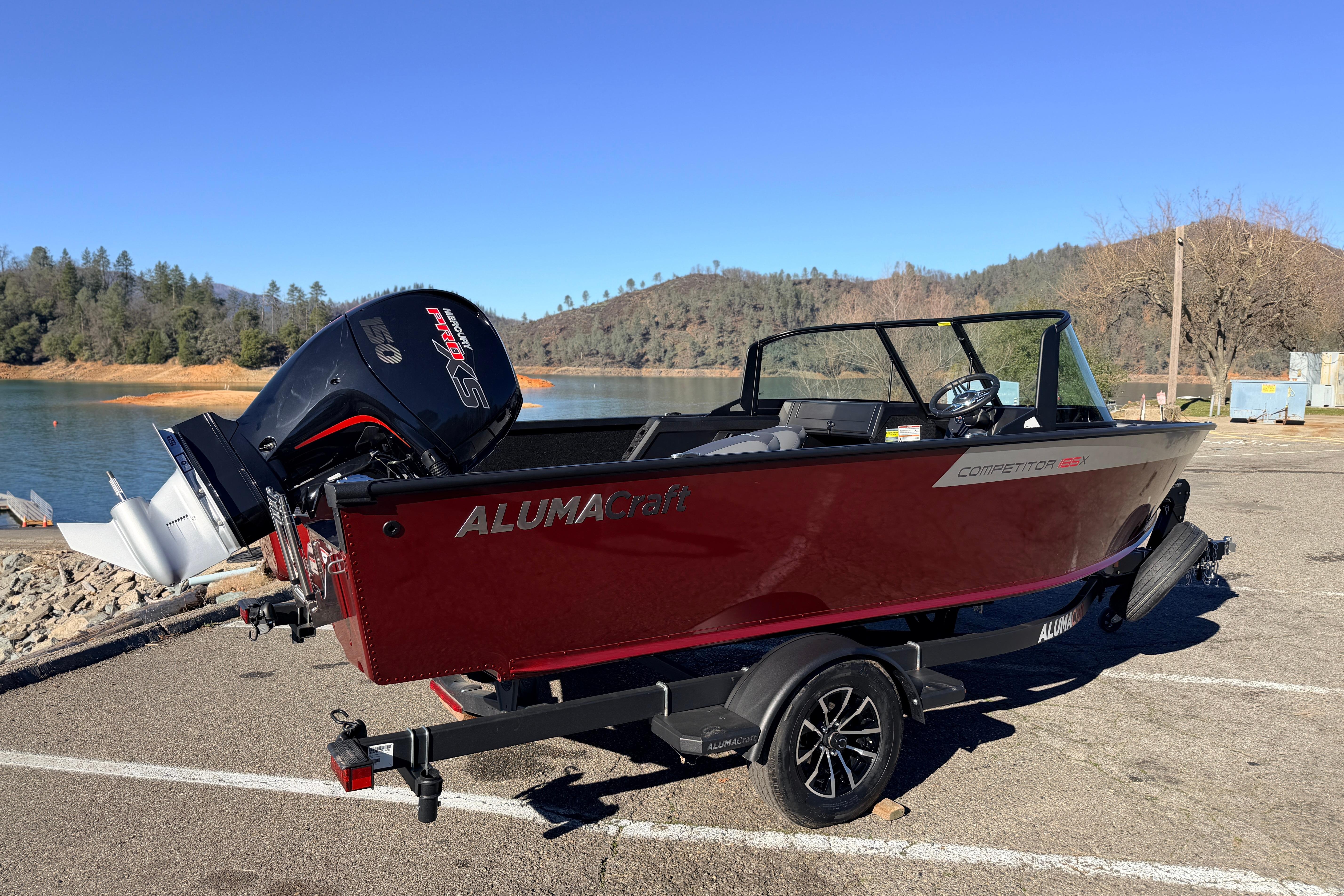 2025 Alumacraft Competitor 185X Sport boat on trailer by a scenic lake.