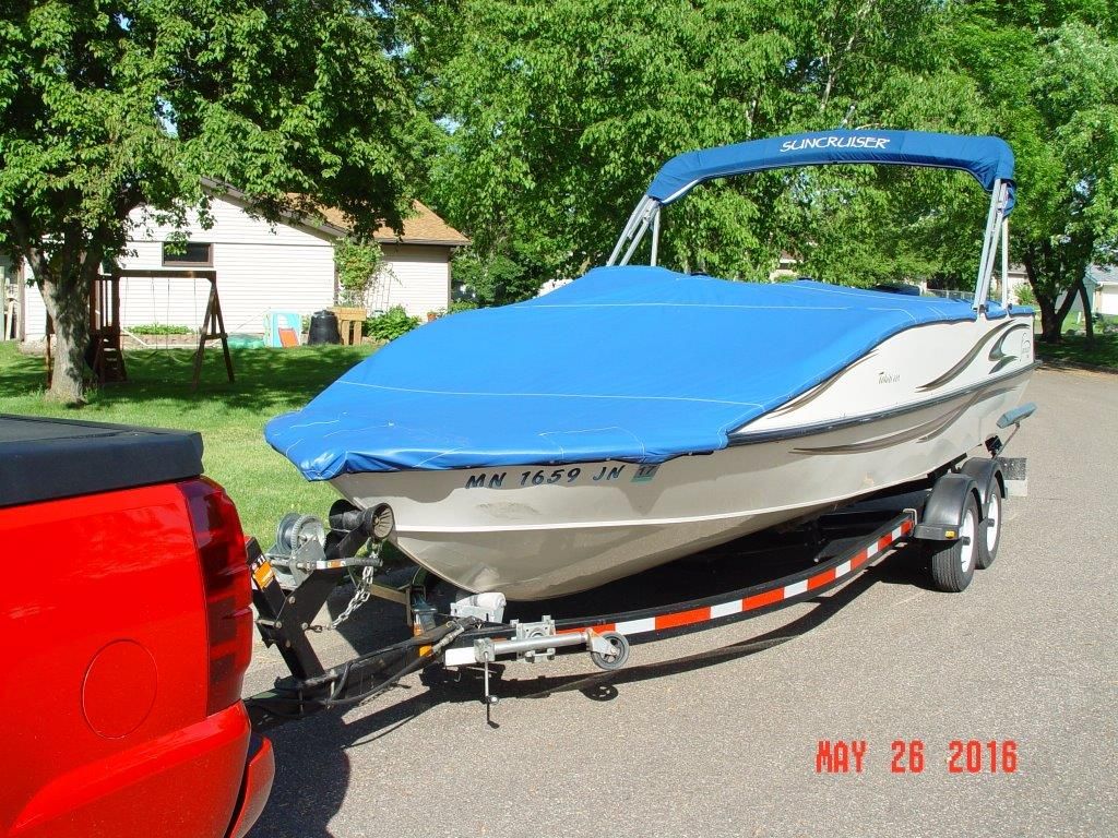 A boat with a blue cover is being towed by a red vehicle on a street.