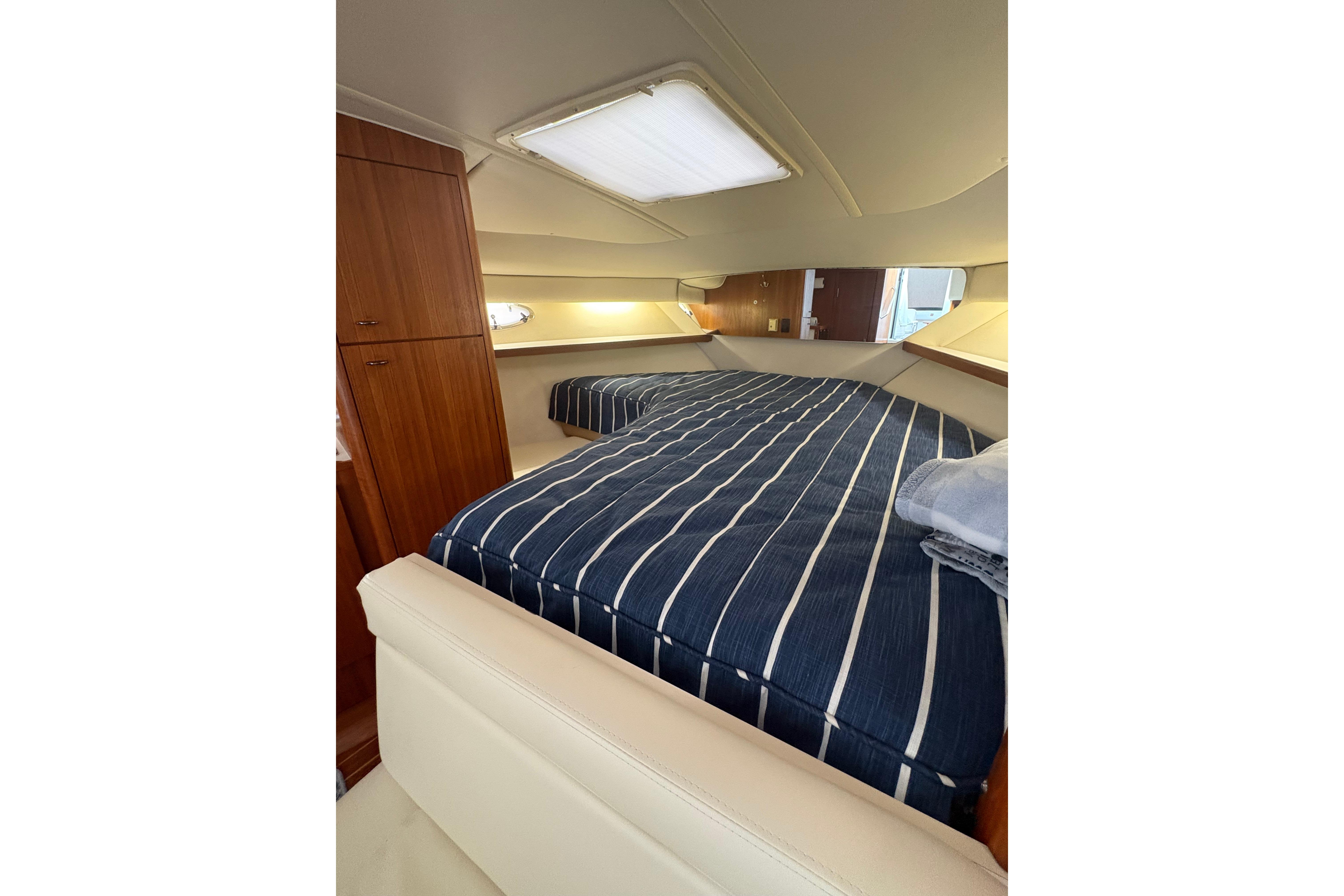 1999 Tiara Yachts 3100 Open cabin interior with striped bedding and wooden cabinetry.