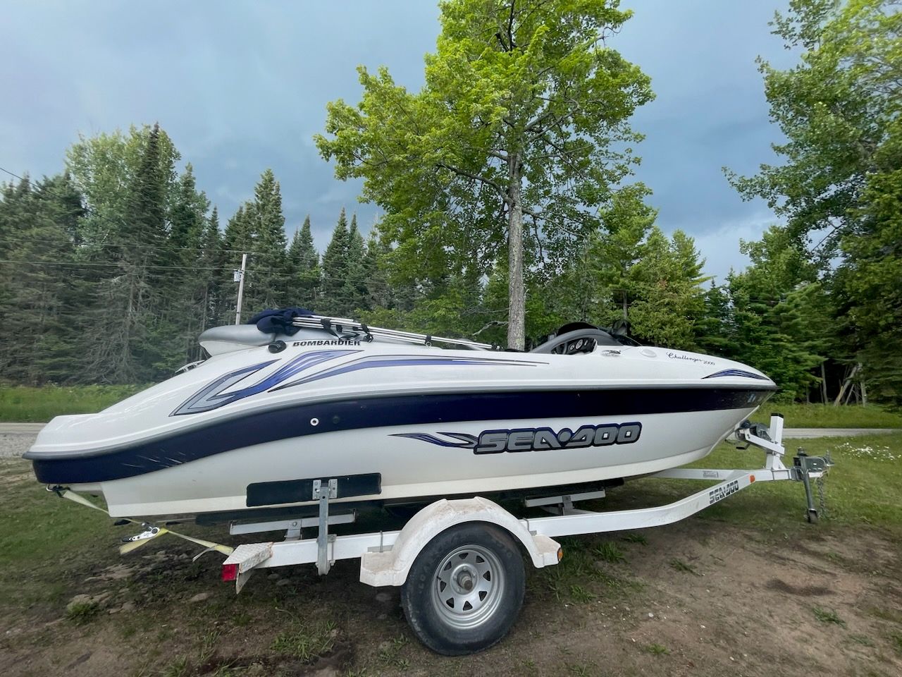 2004 Bombardier Sea-Doo Challenger boat on trailer, surrounded by lush green trees.
