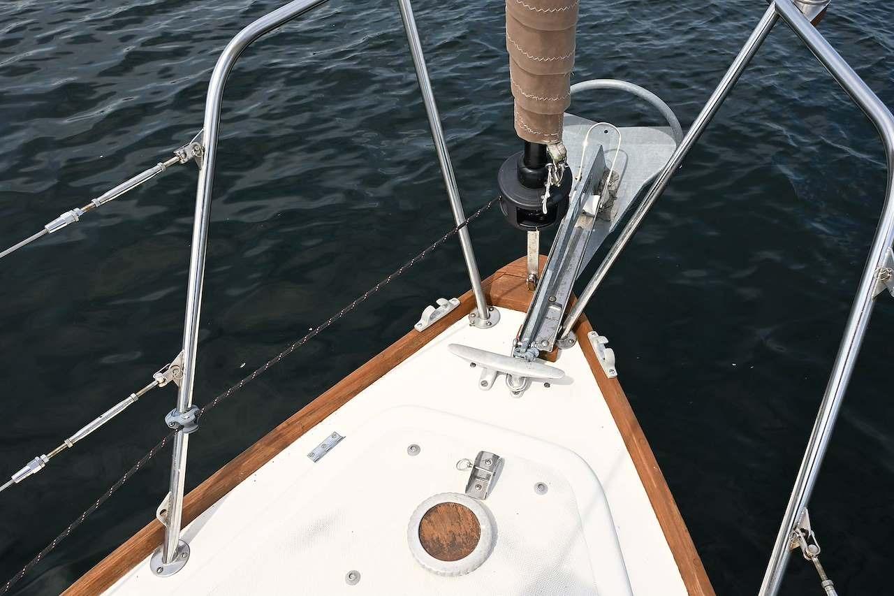 Bow of 1977 Mercator Offshore sailboat with anchor and railing over water.