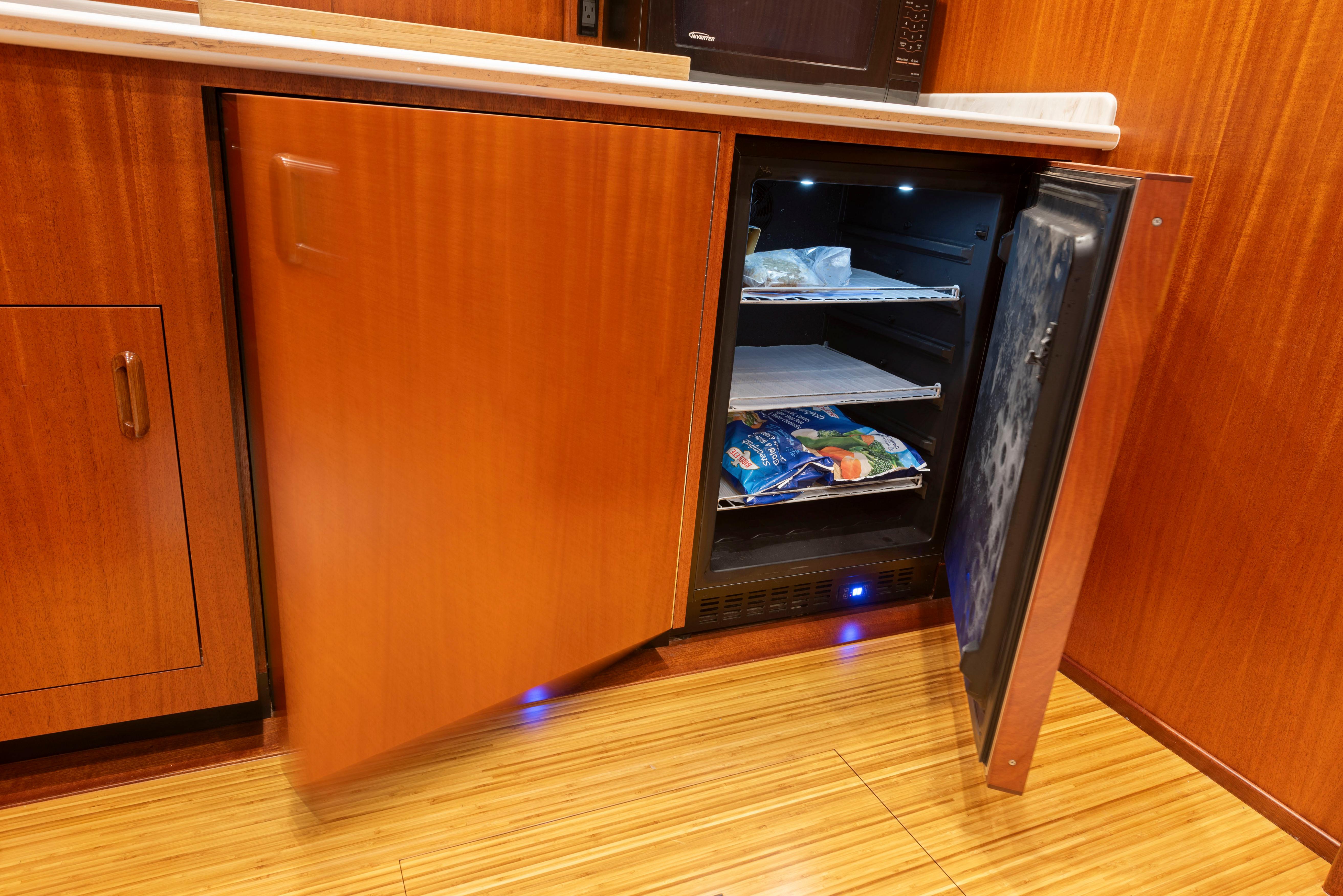 Open mini fridge in 1963 Whiticar 54 Sportfisherman yacht kitchen, wooden cabinetry.