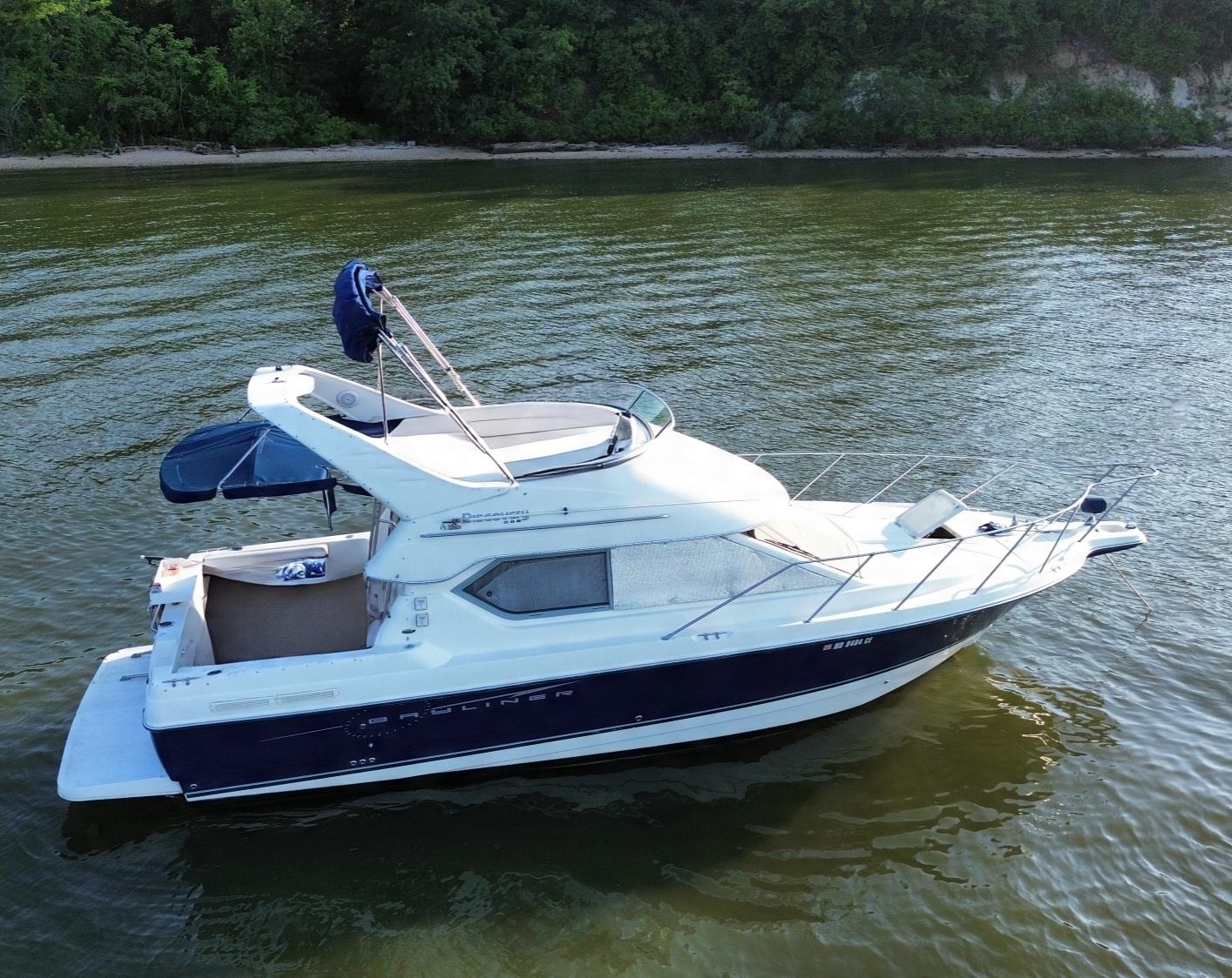 2008 Bayliner Discovery 288 boat on calm water near a forested shoreline.