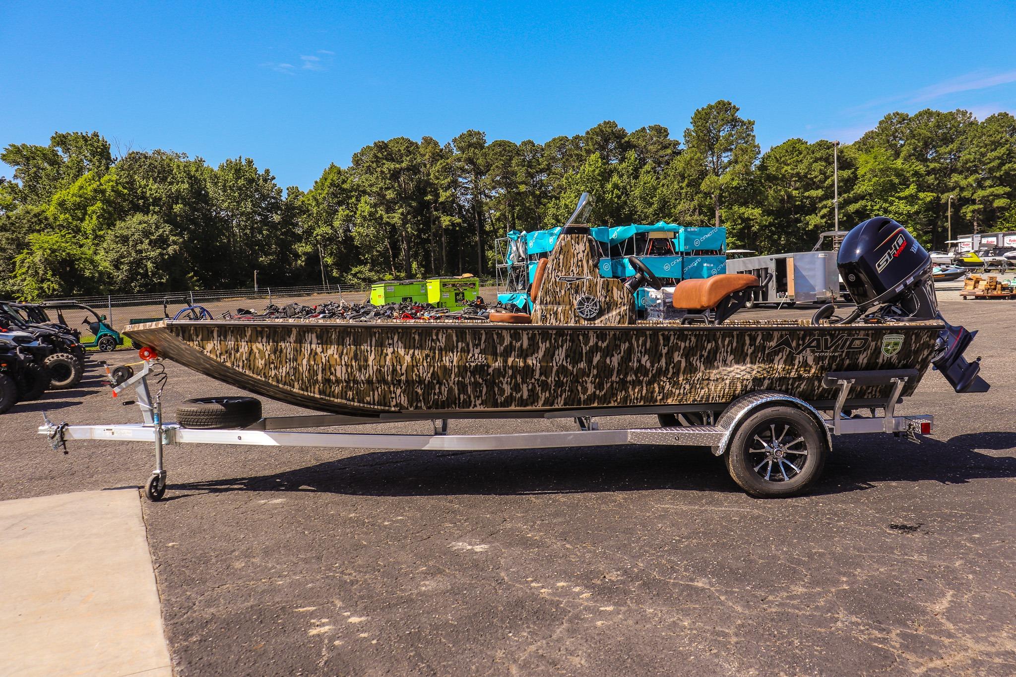 An Avid 20 Rogue CC boat on a trailer, surrounded by trees and vehicles.