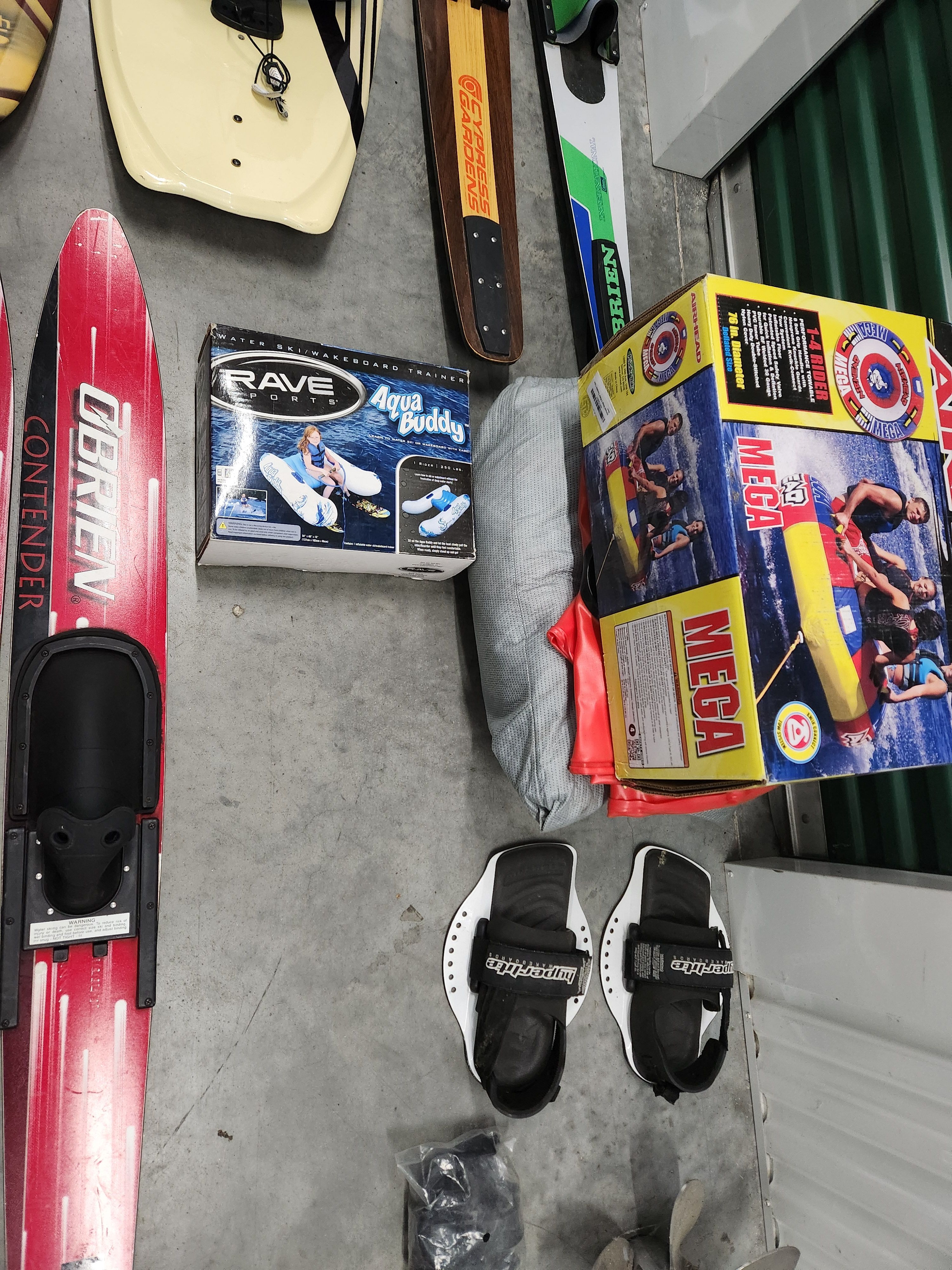 Water sports gear with skis and inflatable tubes on concrete floor.