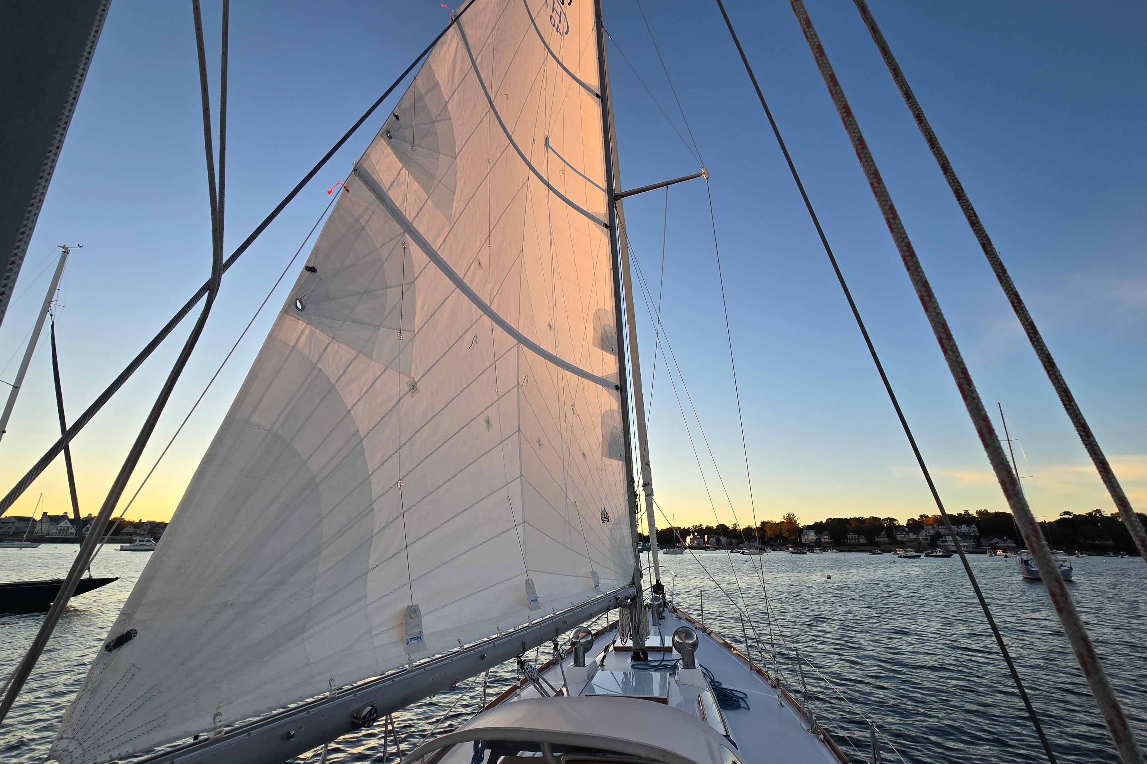 Sailing on a 1970 Hinckley Bermuda 40 at sunset, calm waters, clear sky.