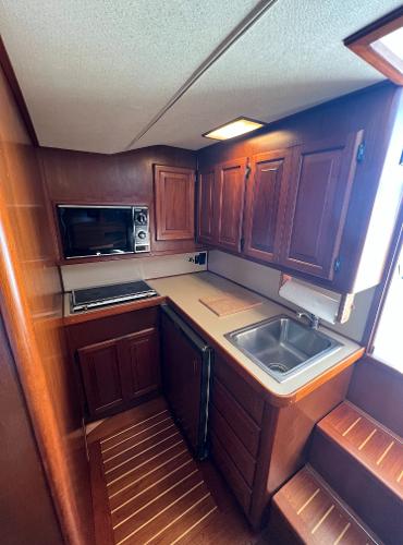 Compact boat kitchen with wooden cabinets, sink, and microwave.