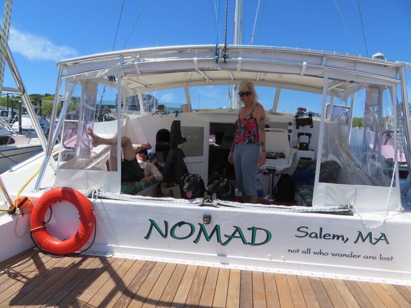A woman stands on a catamaran named "NOMAD" docked in Salem, MA.