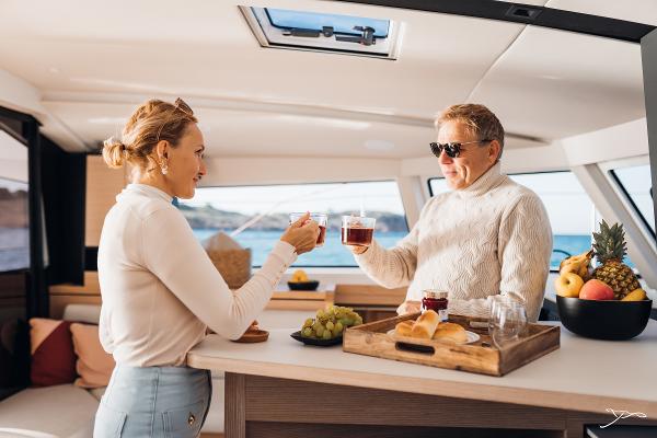 Couple enjoying drinks on a 2025 Nautitech 44 Open yacht, with fruit and snacks.