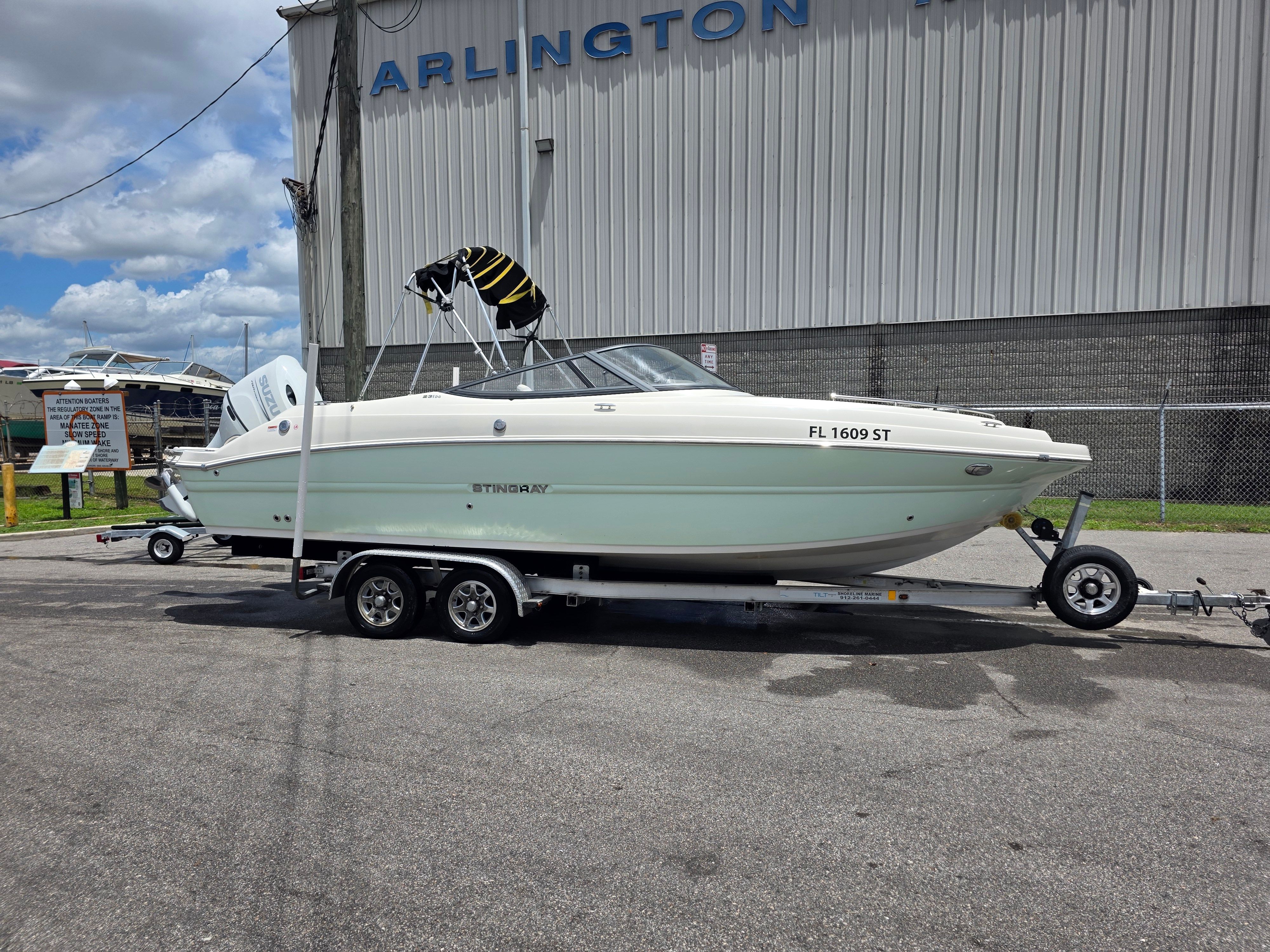 A white Stingray 231 DC boat on a trailer in front of a building.