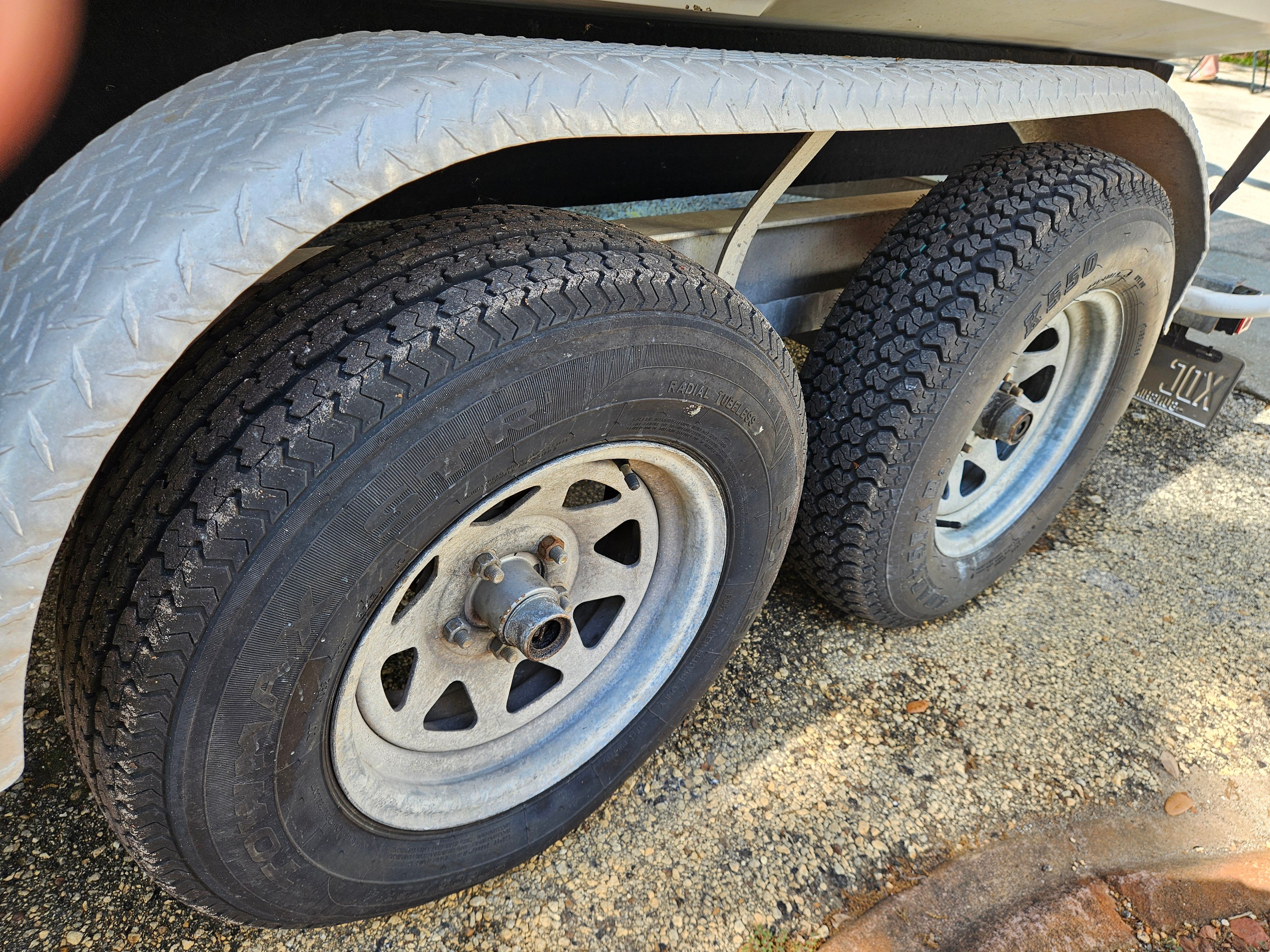 Close-up of two trailer wheels with rugged tread on a gravel path.