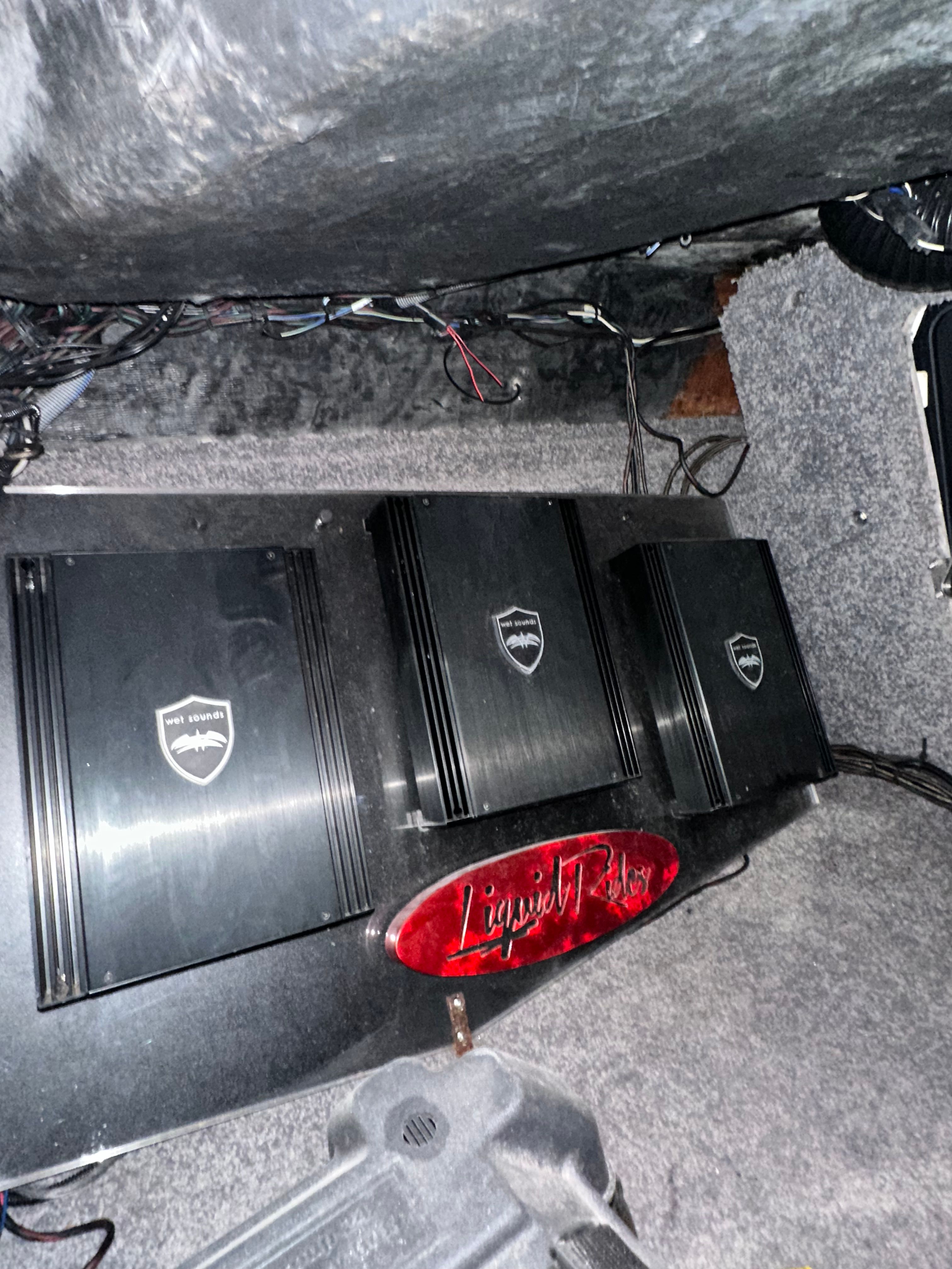 Three black amplifiers are installed in a boat, surrounded by gray carpeting.