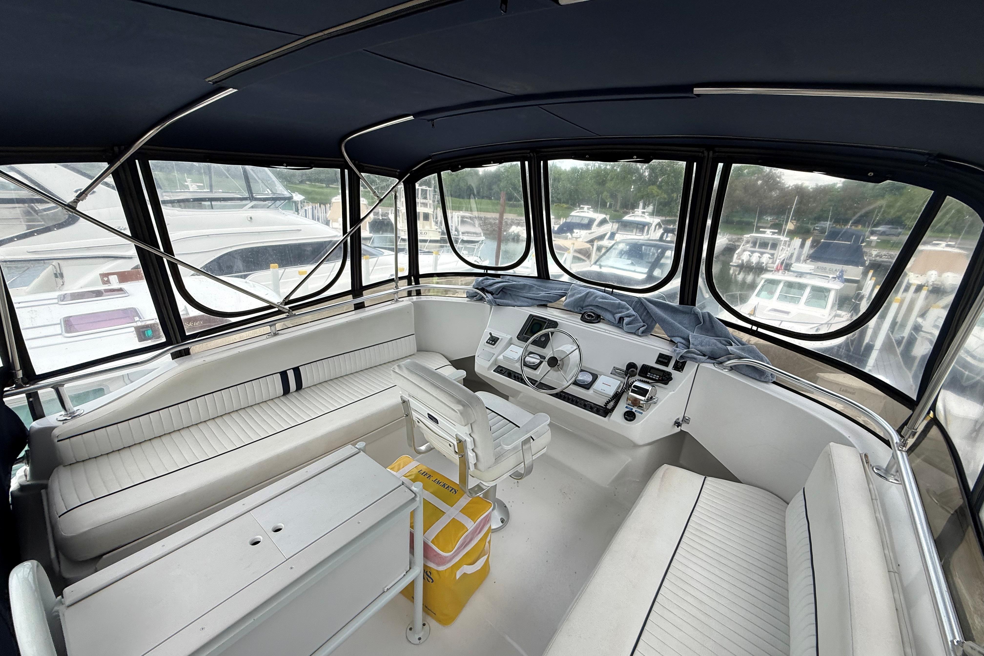 1999 Mainship 350 Trawler helm with panoramic marina view, featuring white seating and controls.