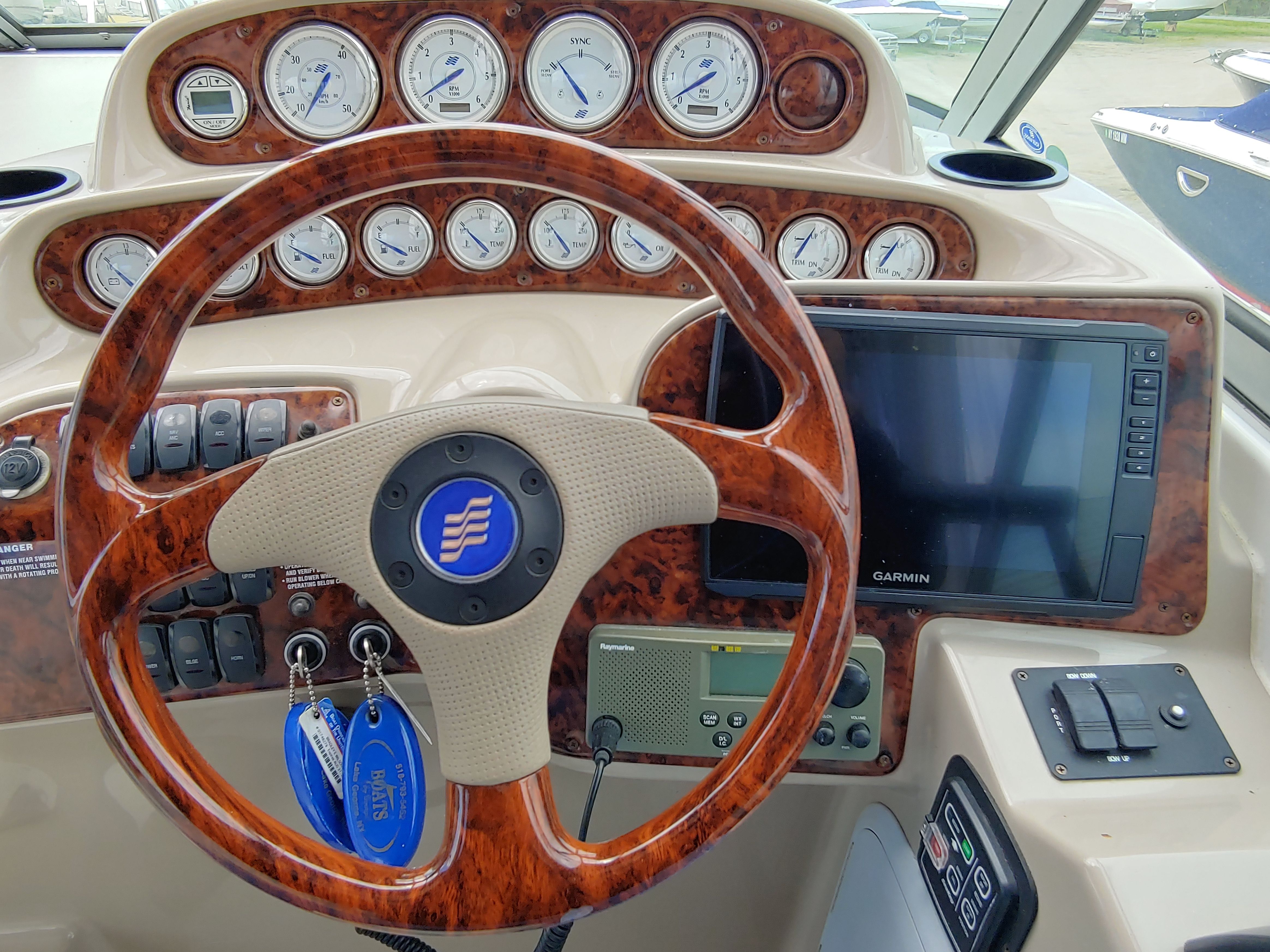 The cockpit of a boat with a wooden steering wheel, instrument gauges, and a Garmin navigation system.