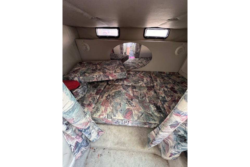 Interior cabin of a 1997 Crownline 250 CR boat with patterned cushions and small windows.
