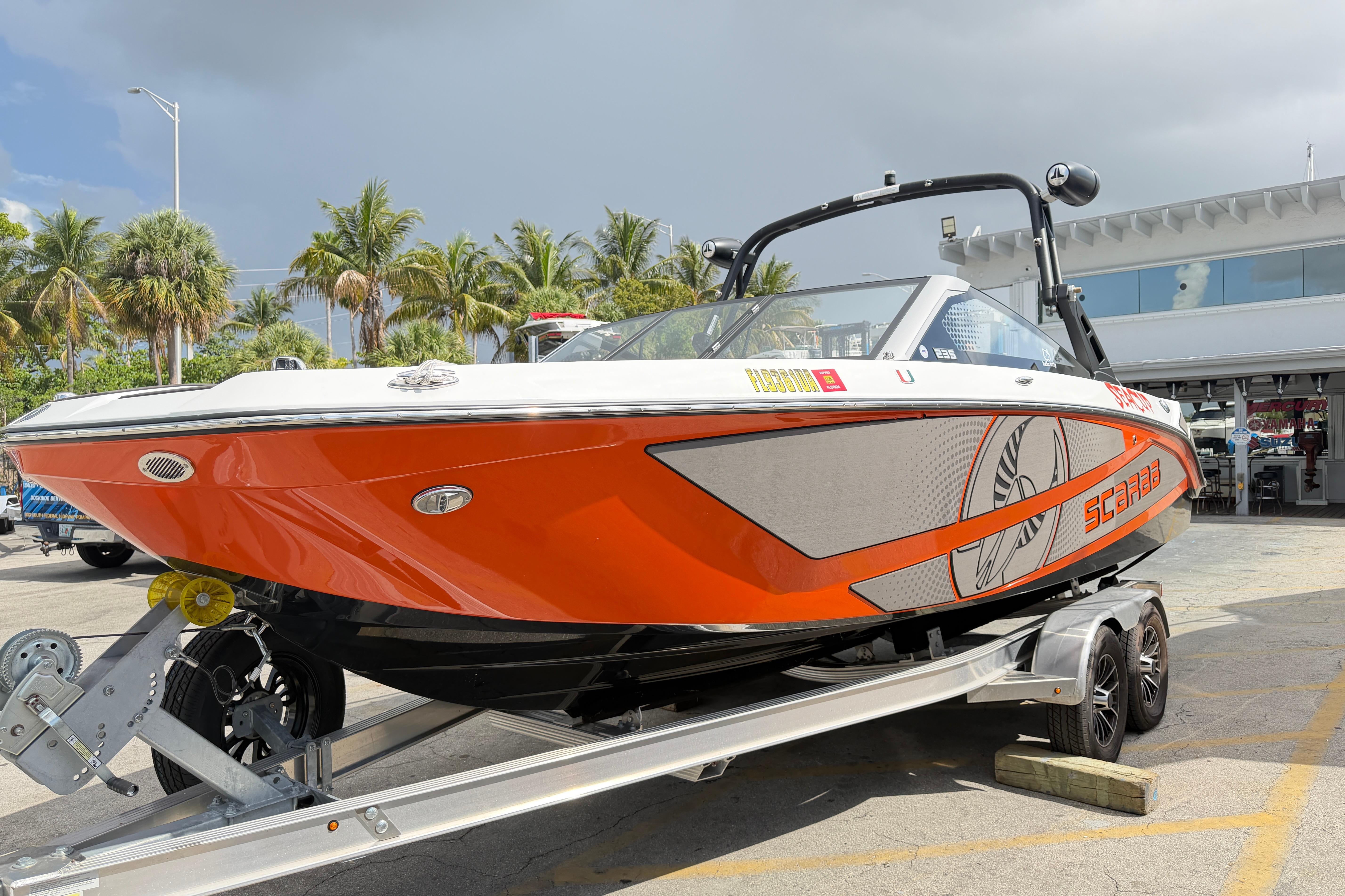 2026 Scarab 235 LX boat in vibrant orange on a trailer, surrounded by palm trees.