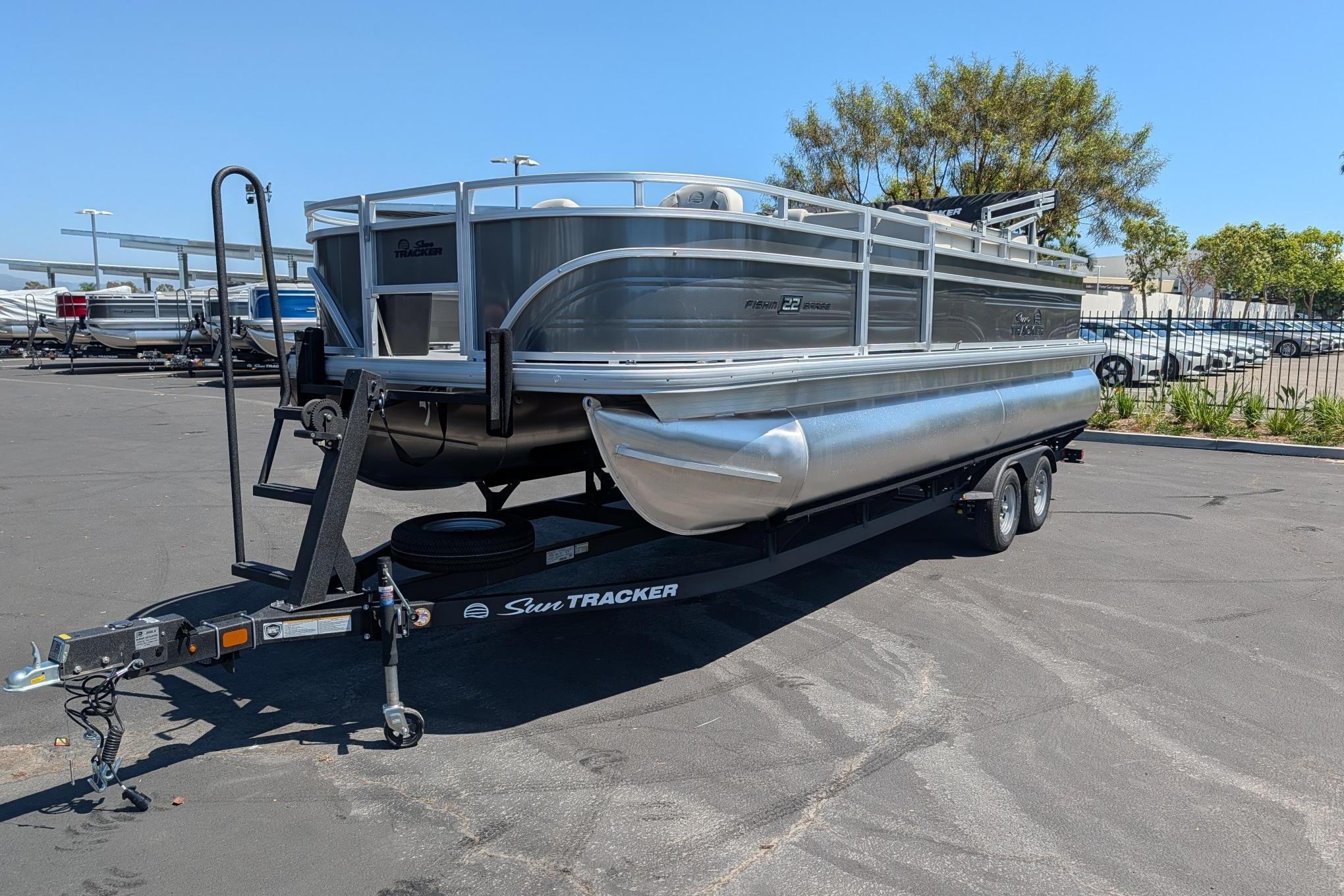 2026 Sun Tracker Fishin' Barge 22 DLX pontoon boat on trailer in parking lot.
