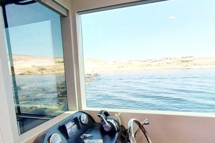 Boat interior with control panel overlooking serene waters and distant shoreline, Adonia Galileo Trip 2023.