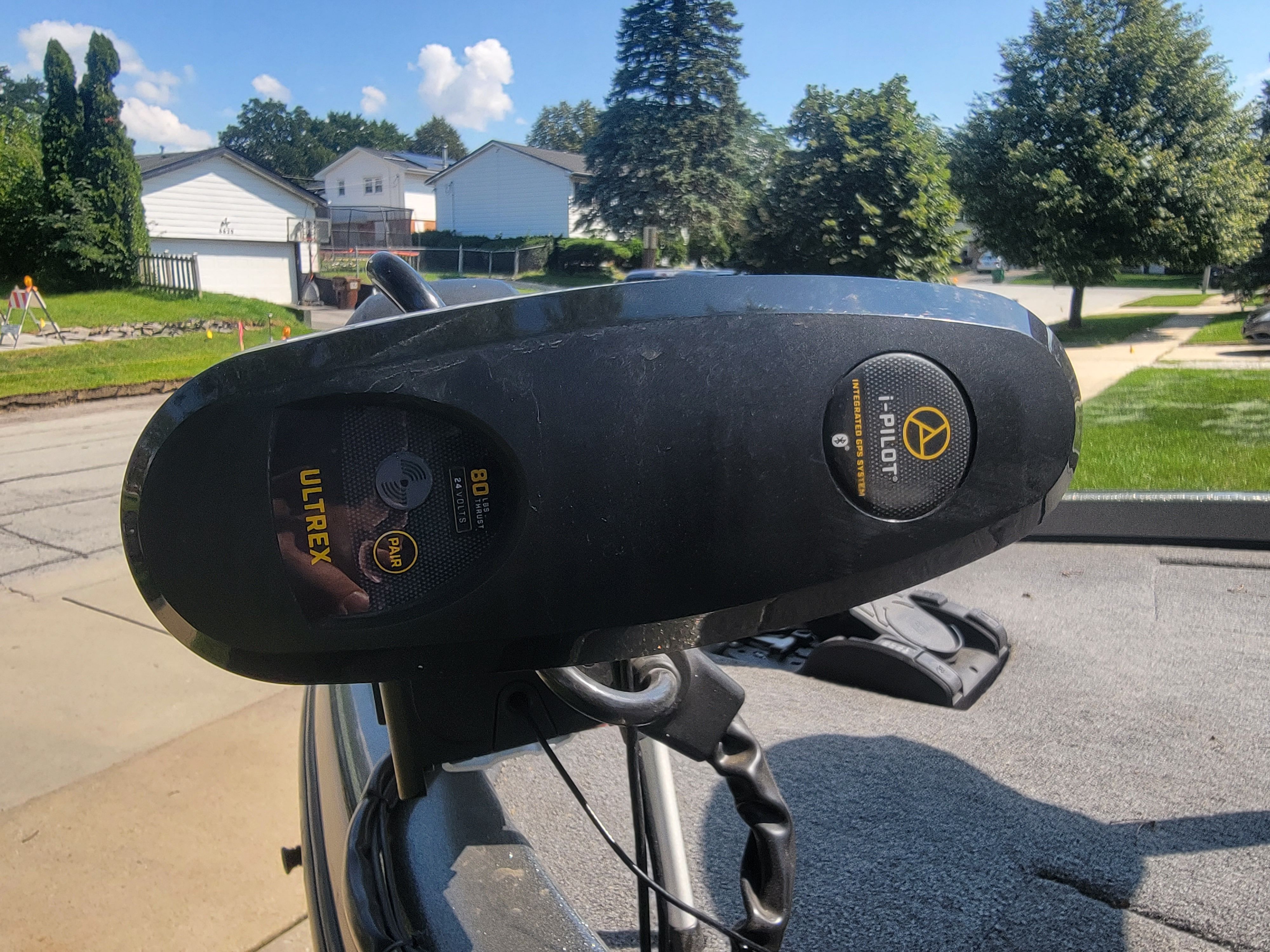 Close-up of a boat motor with i-Pilot and Ultrex logo, on a trailer in a residential area.