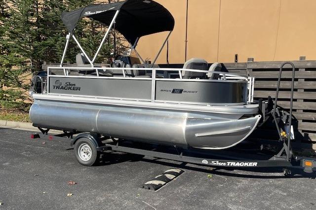 2026 Sun Tracker Bass Buggy 16 XL Select pontoon boat on trailer, parked outdoors.