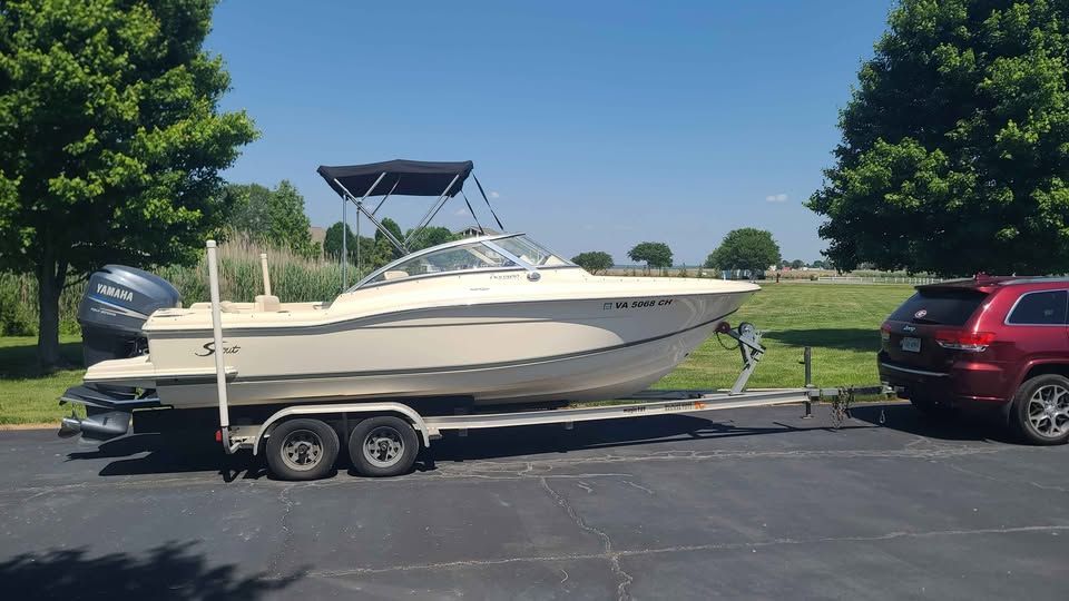 A 2005 Scout 222 Dorado boat on a trailer, towed by a red SUV.