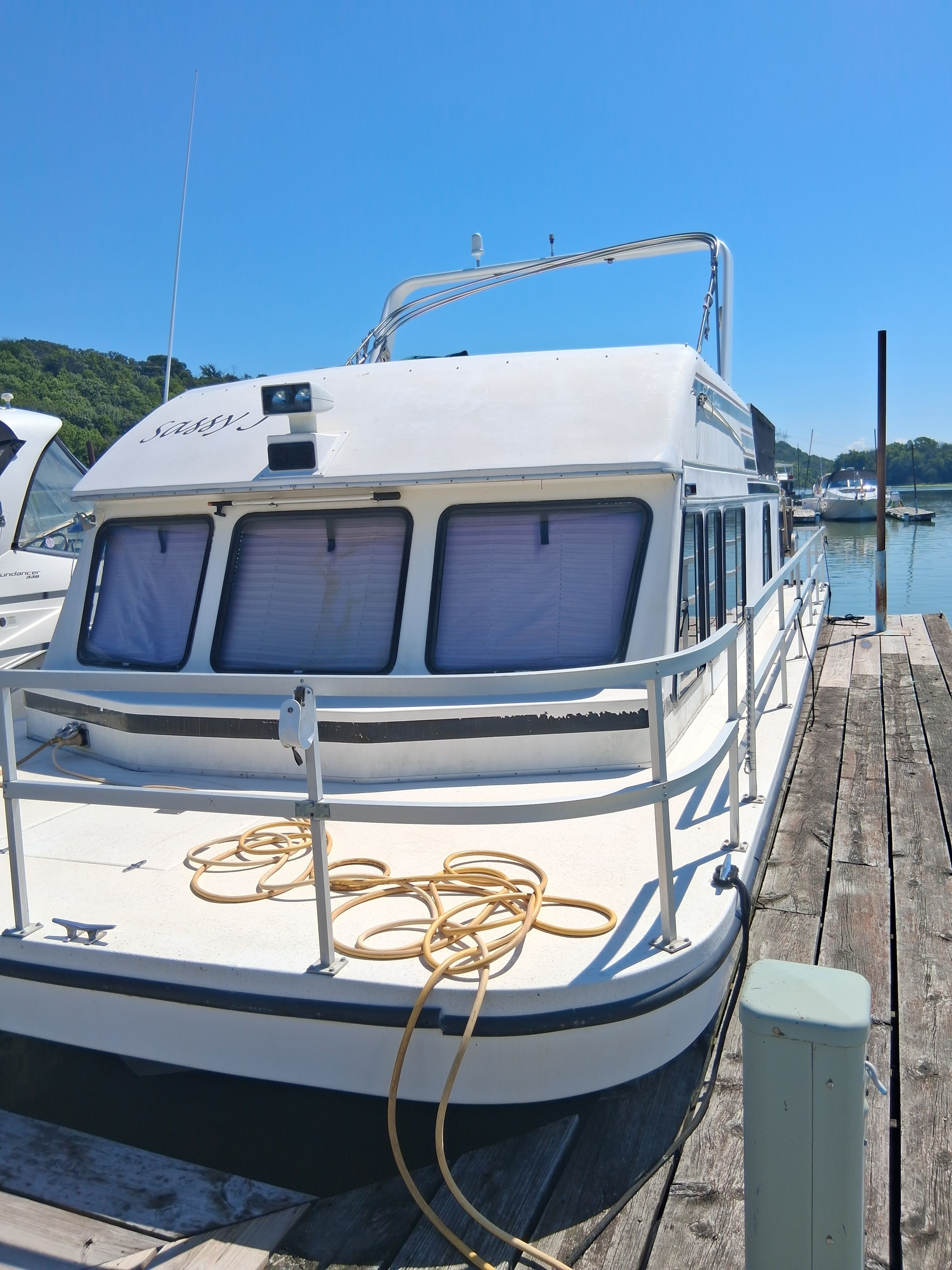 A 1993 Gibson 370 Sport docked at a wooden pier. It features a spacious deck and windows with blinds.