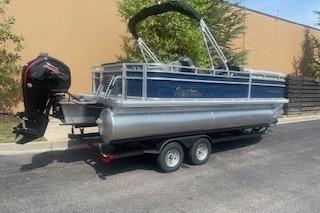 2026 Sun Tracker SportFish 20 DLX pontoon boat on trailer, parked outdoors.